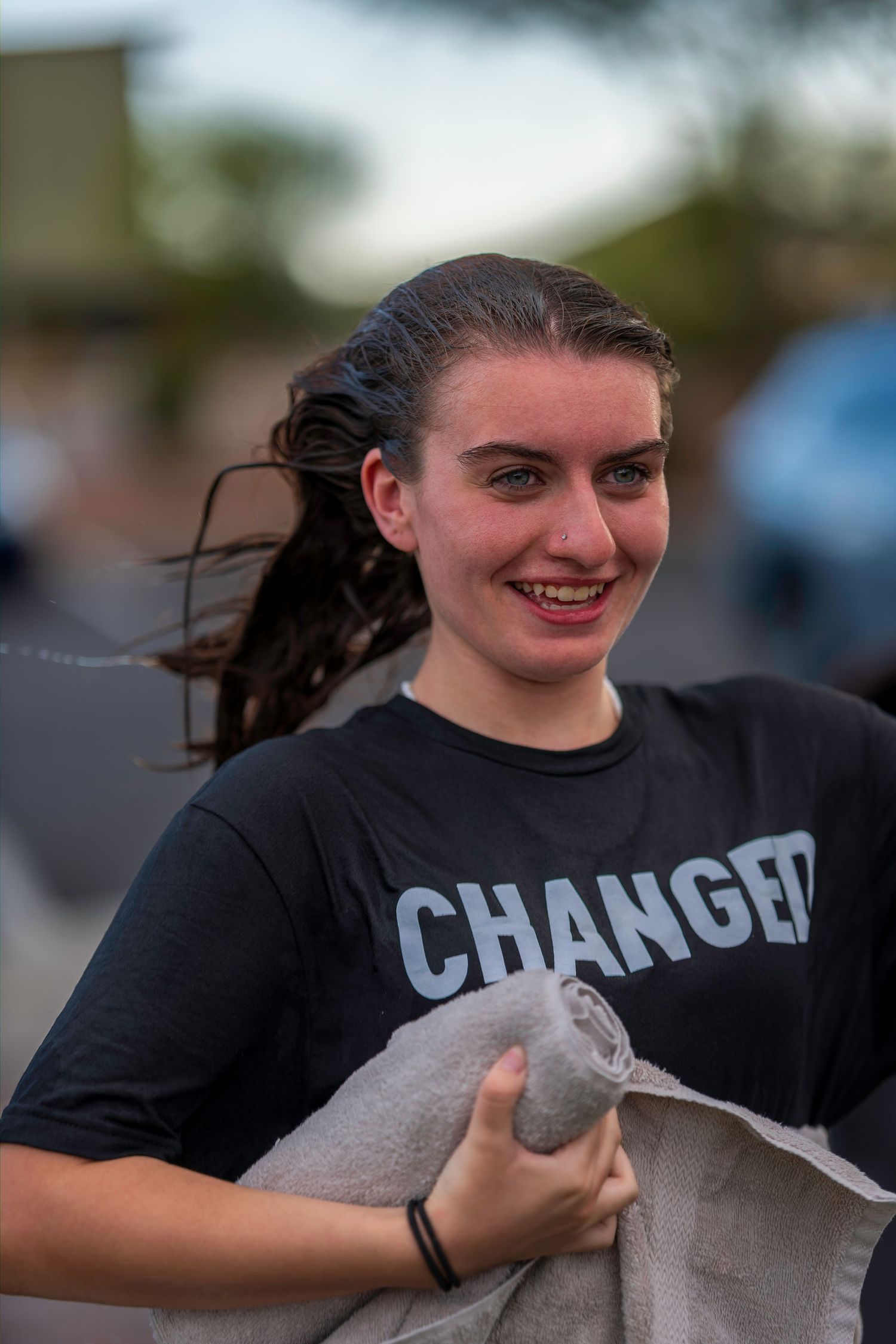 Smiling young woman with wet hair holding a towel after baptism, wearing a black Changed shirt.