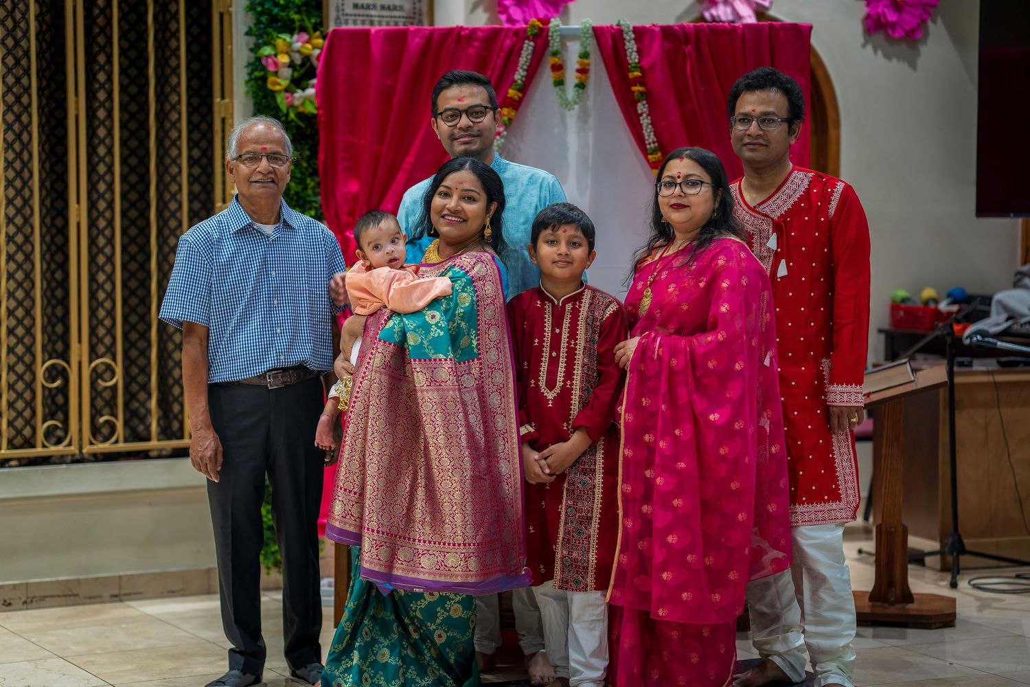 Family group photo at a South Asian celebration, wearing traditional colorful attire including pink and green outfits.
