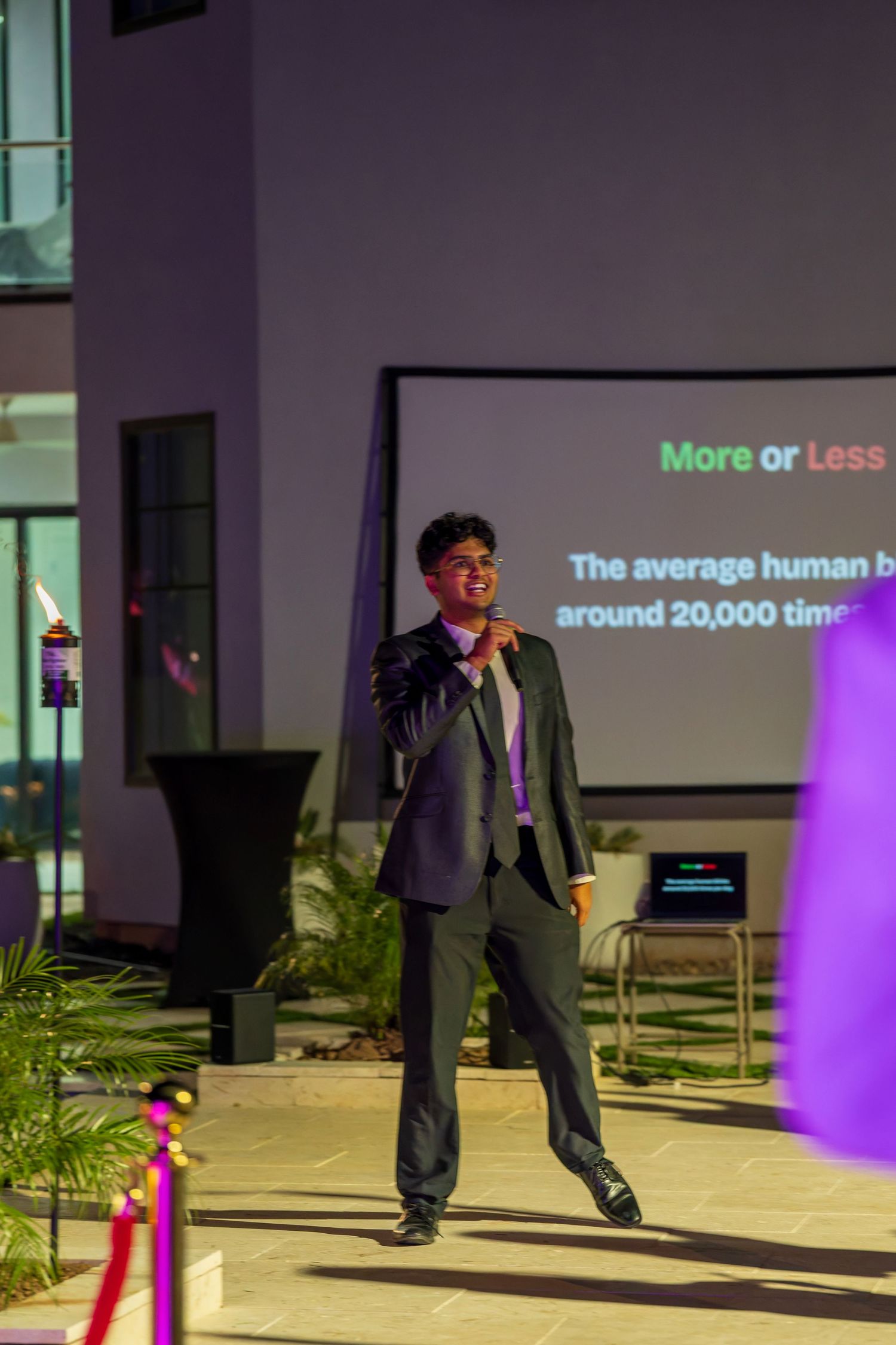 A presentation screen displays text while speakers stand on a dimly lit outdoor stage.