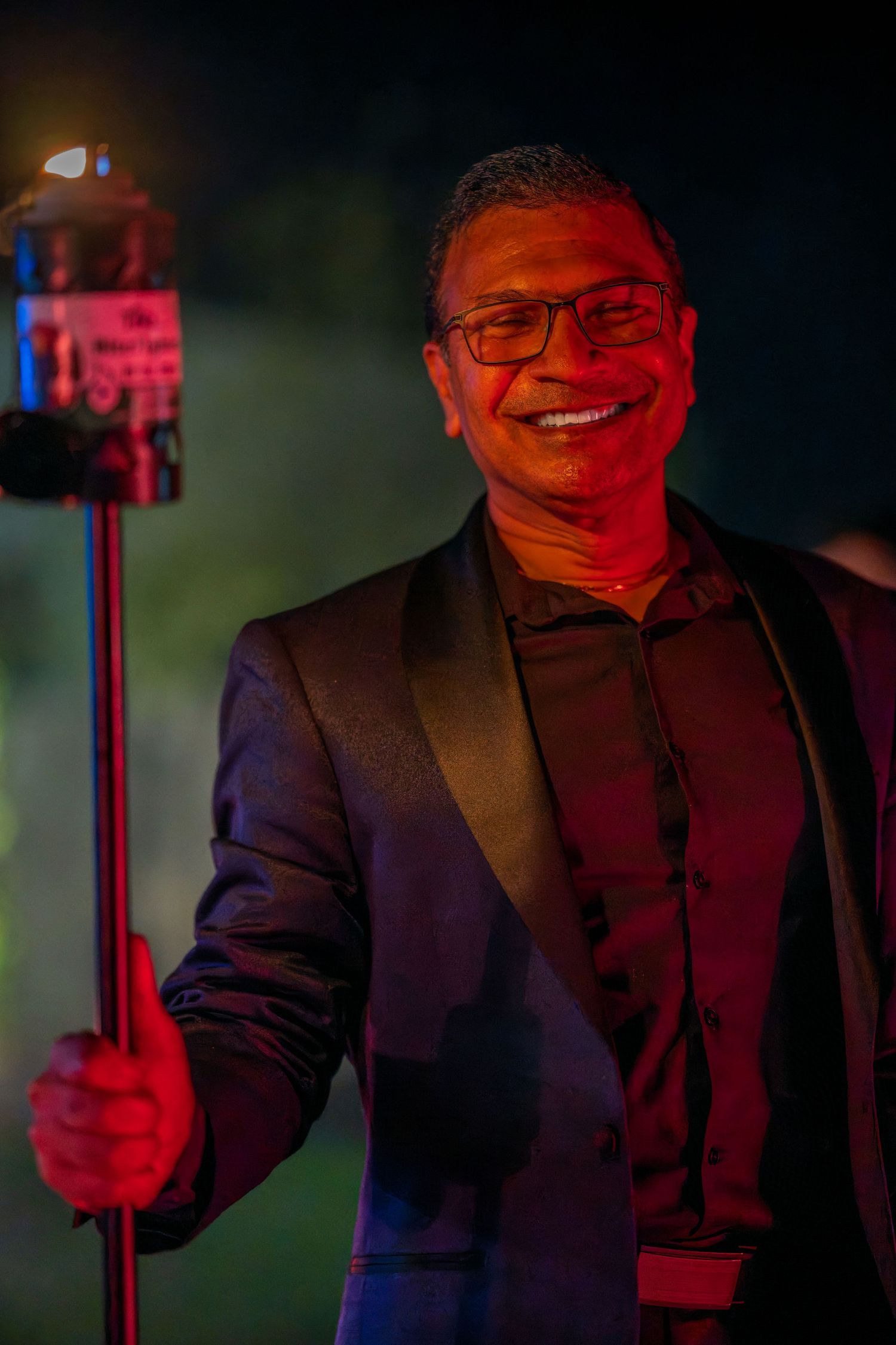 A person in formal attire holds a sparkler while smiling during an evening celebration.