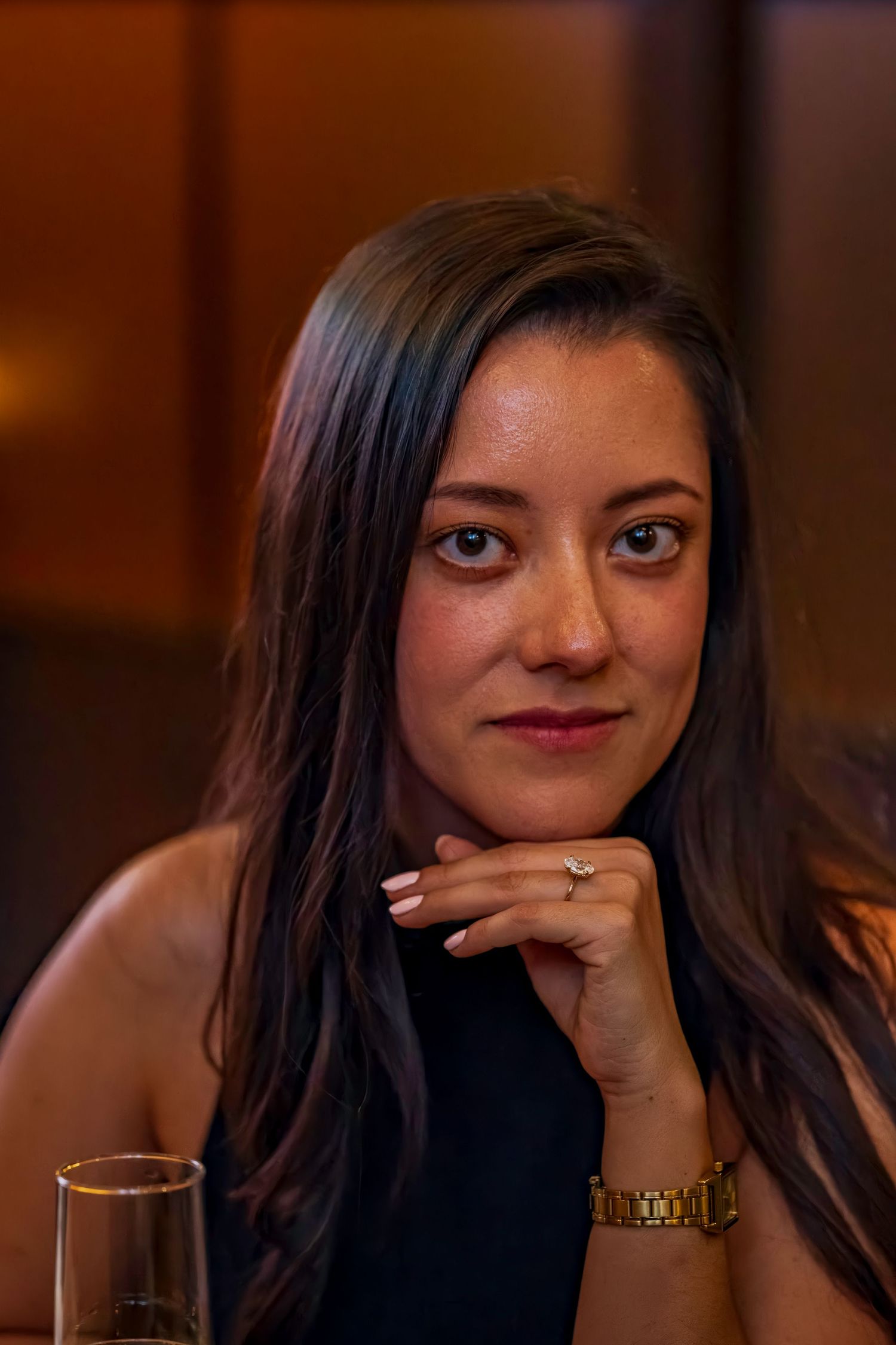 A portrait of a woman with long dark hair wearing a black top and gold watch.