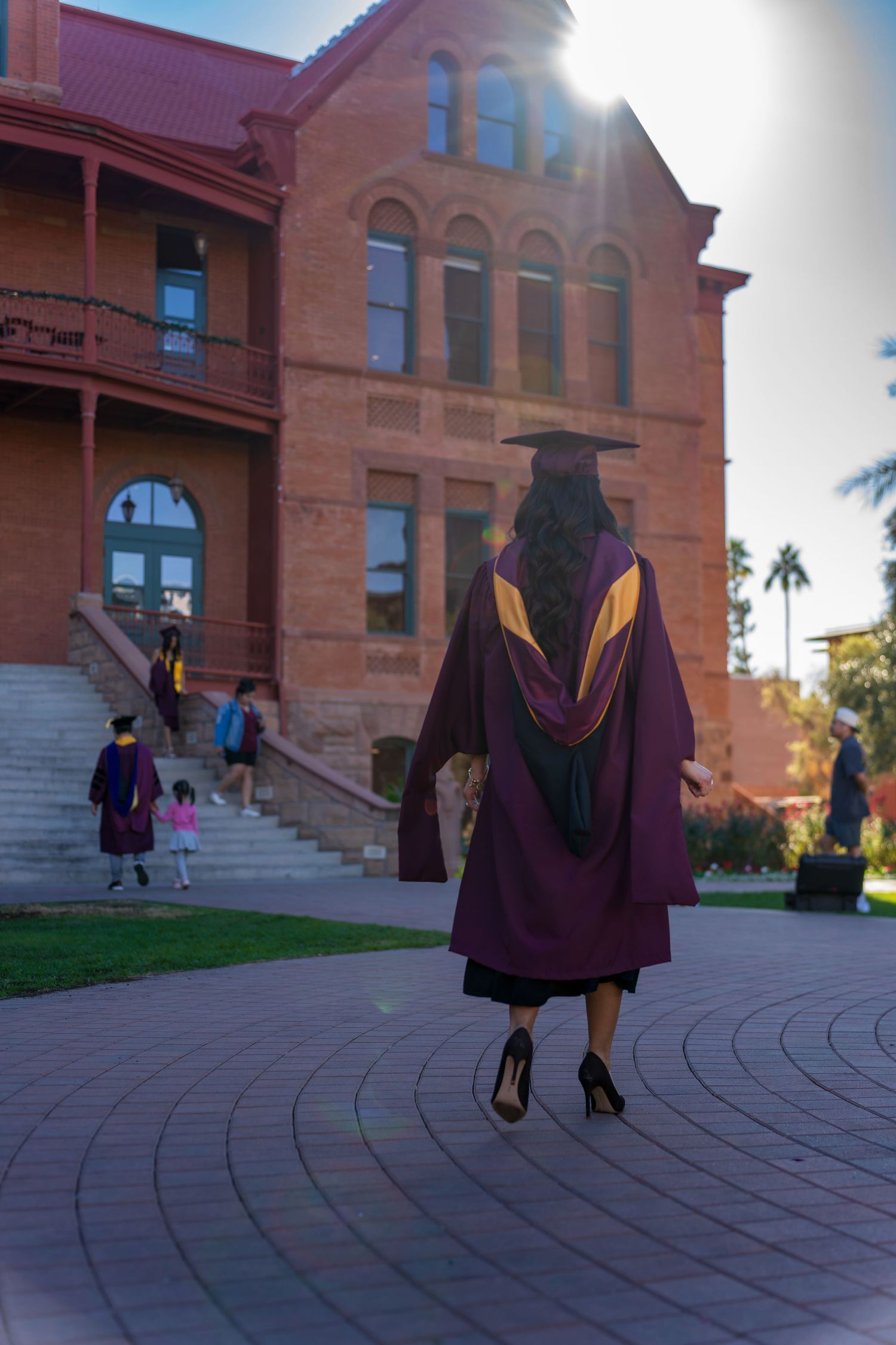 Low angle view of graduate walking on brick pavement with historic building in background.