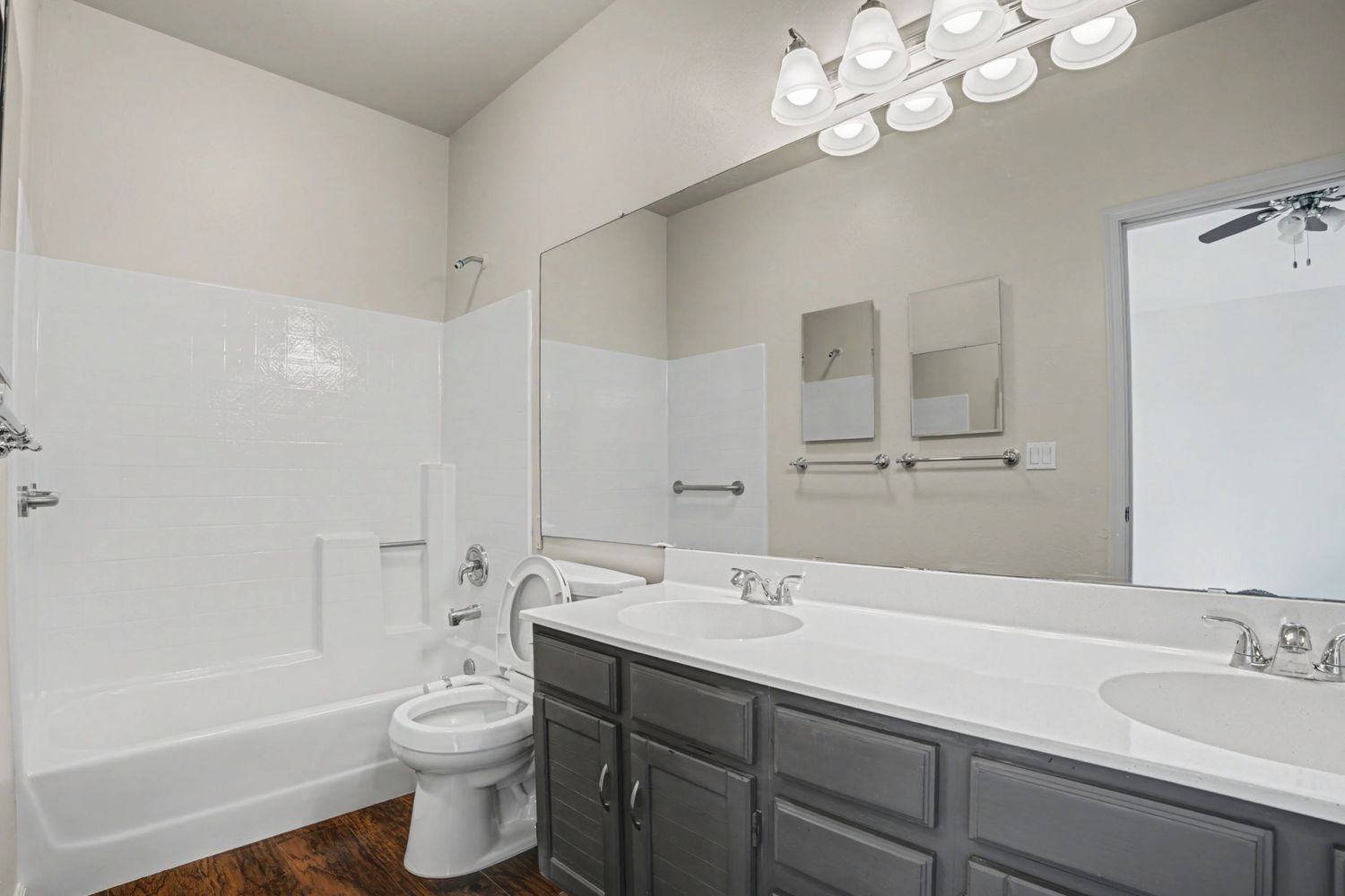 Spacious bathroom with double sink vanity, dark cabinets, white countertops, large mirror, and tub-shower combo.
