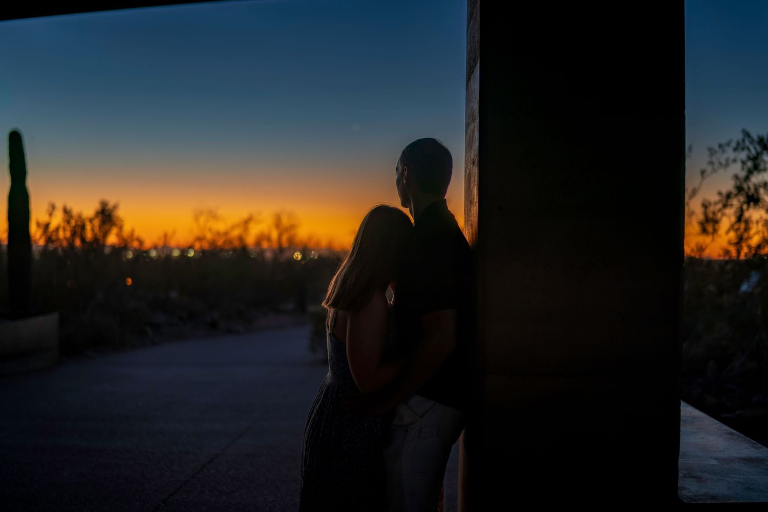 Silhouette of a person leaning against a pillar watching a vibrant desert sunset with cacti.