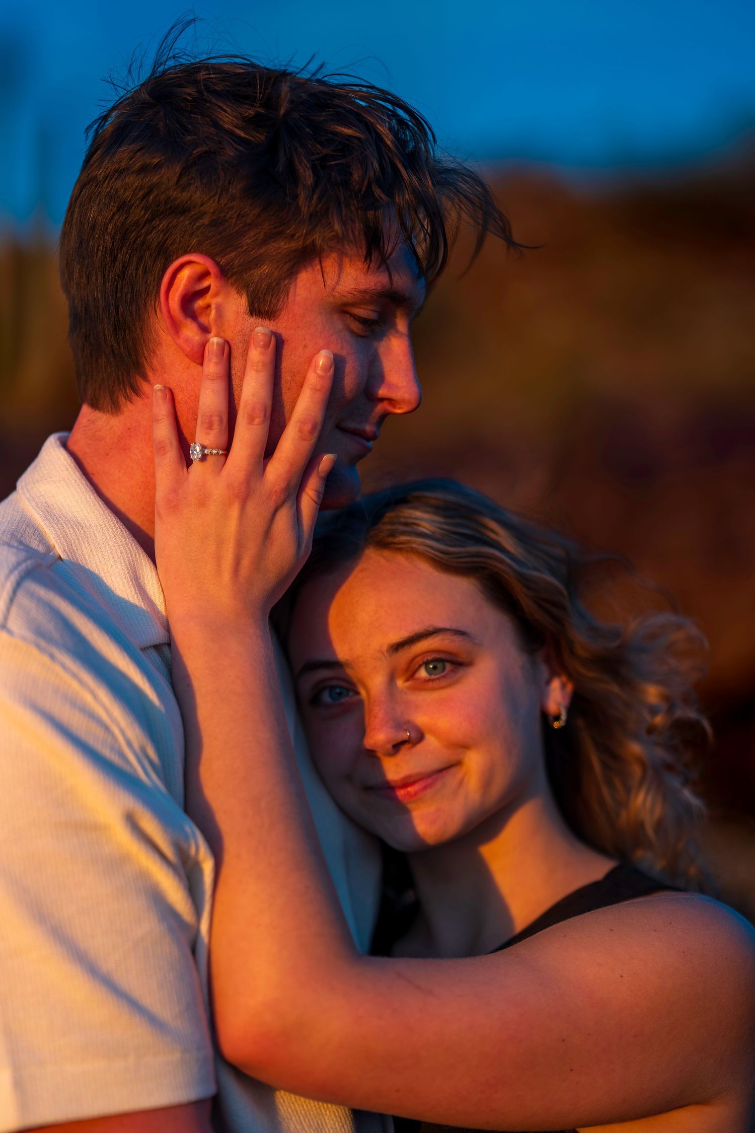 Woman tenderly cupping mans face while embracing during warm golden hour desert light.