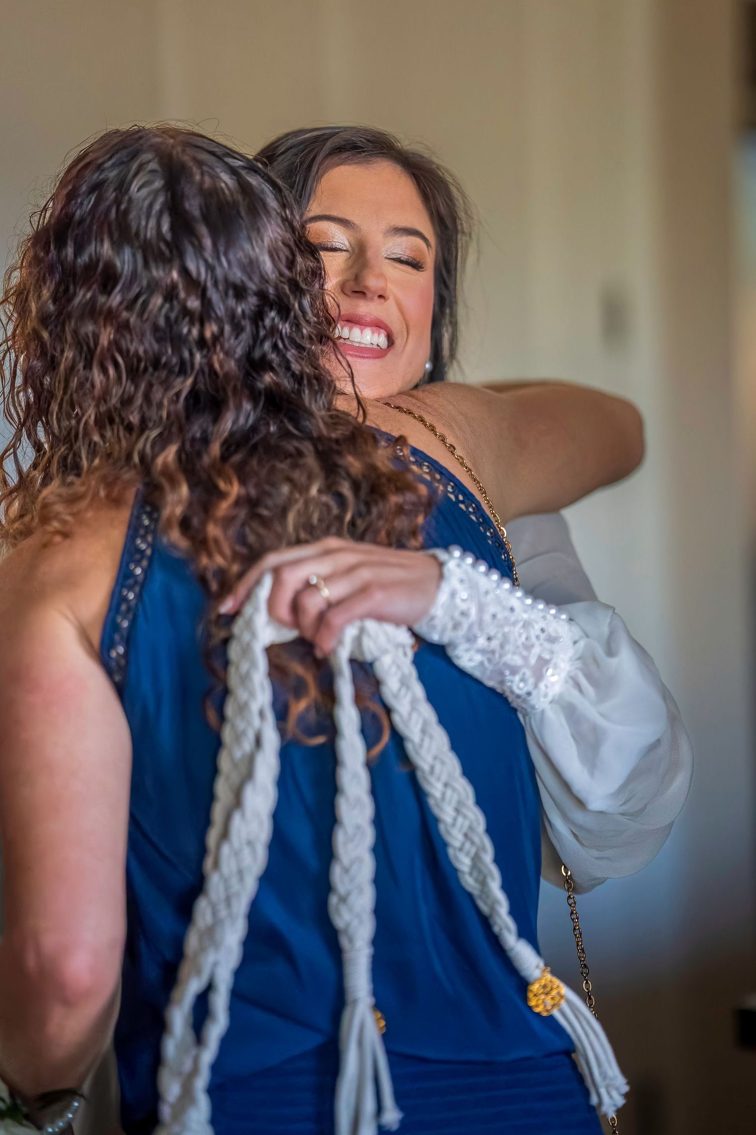 Bride in white gown shares joyful hug with woman in blue dress at wedding celebration.