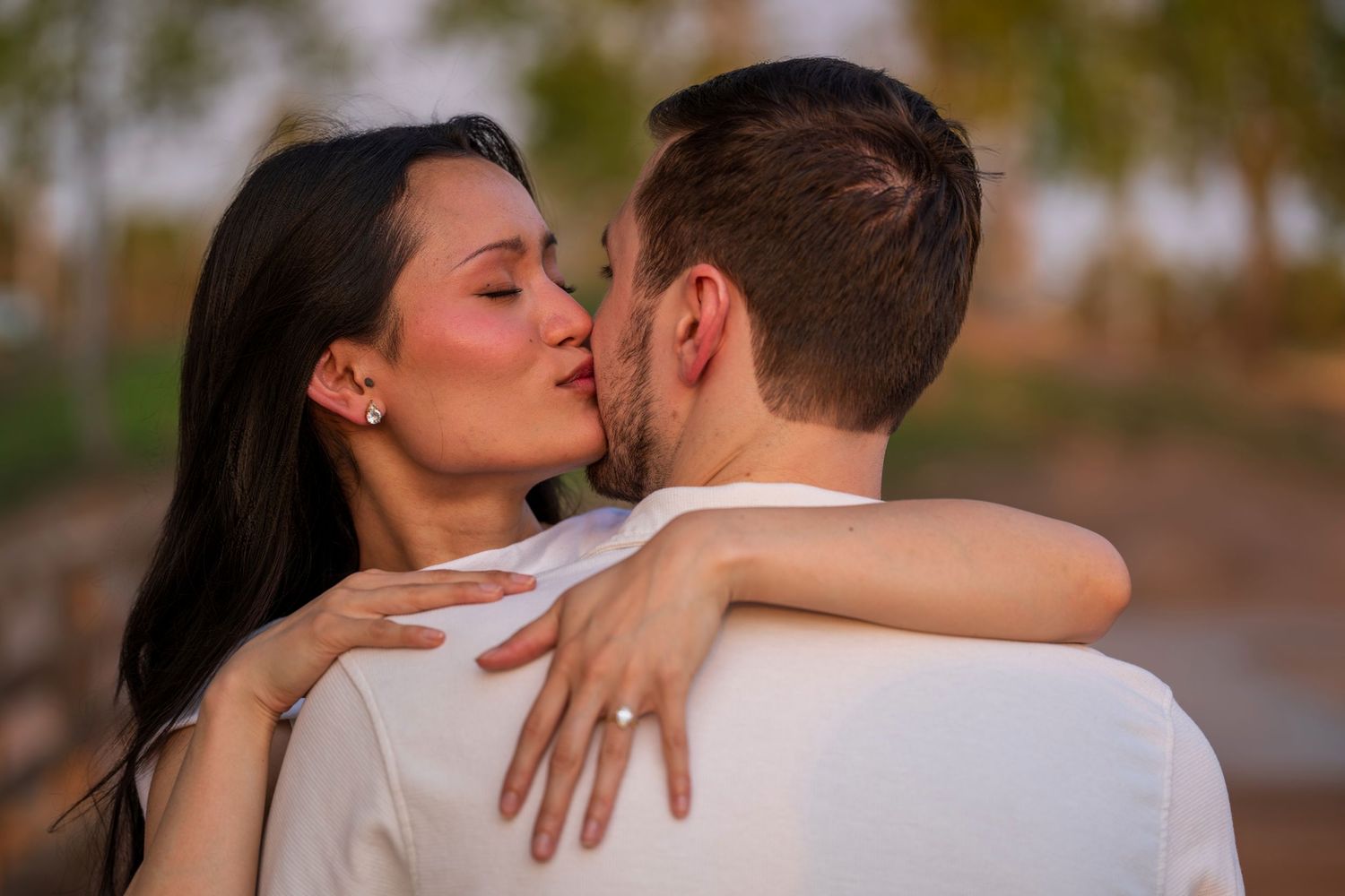 Couple sharing a romantic kiss during golden hour engagement or wedding photo session outdoors.