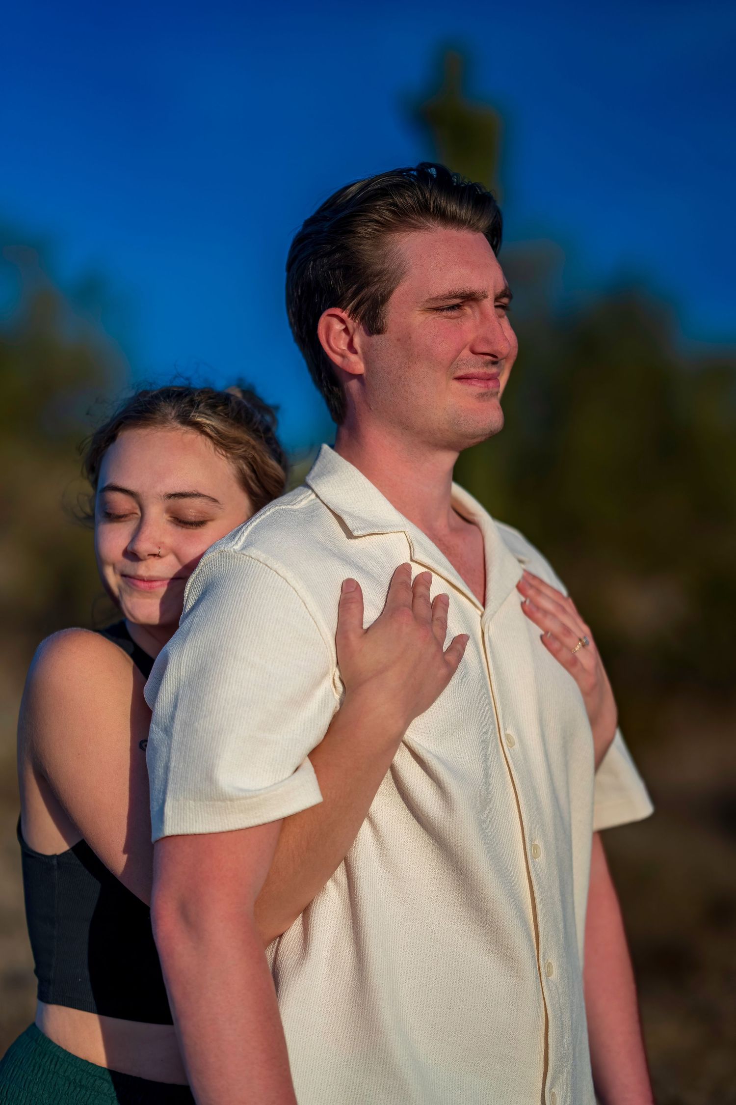 Young couple in tender embrace at sunset, woman resting head on mans back.