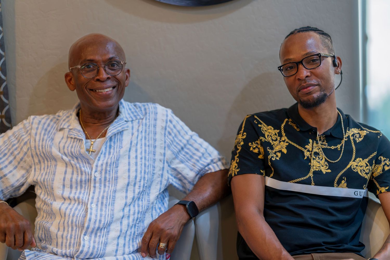 Two men sit together on a couch, sharing a warm moment.