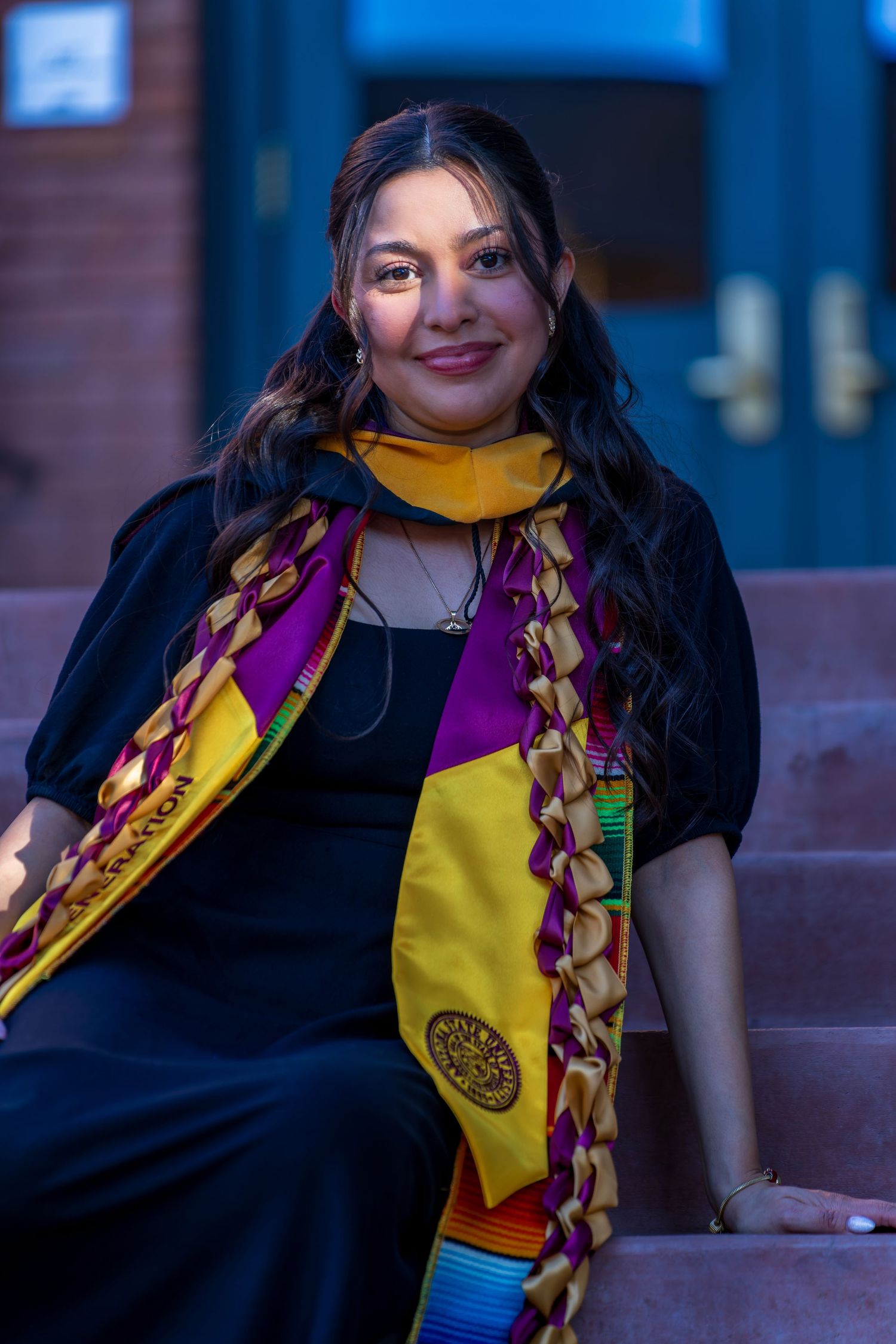 Close-up portrait of graduate wearing black gown with yellow and maroon graduation stole.