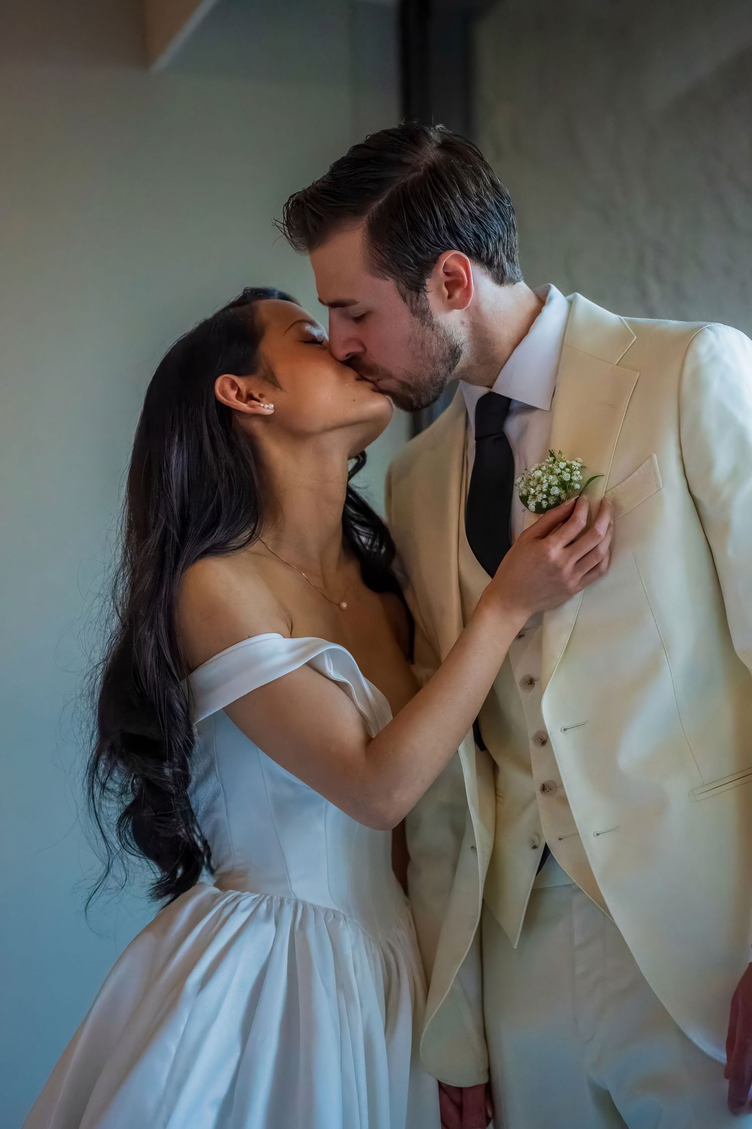 A romantic wedding couple shares an intimate kiss in elegant white and cream attire.