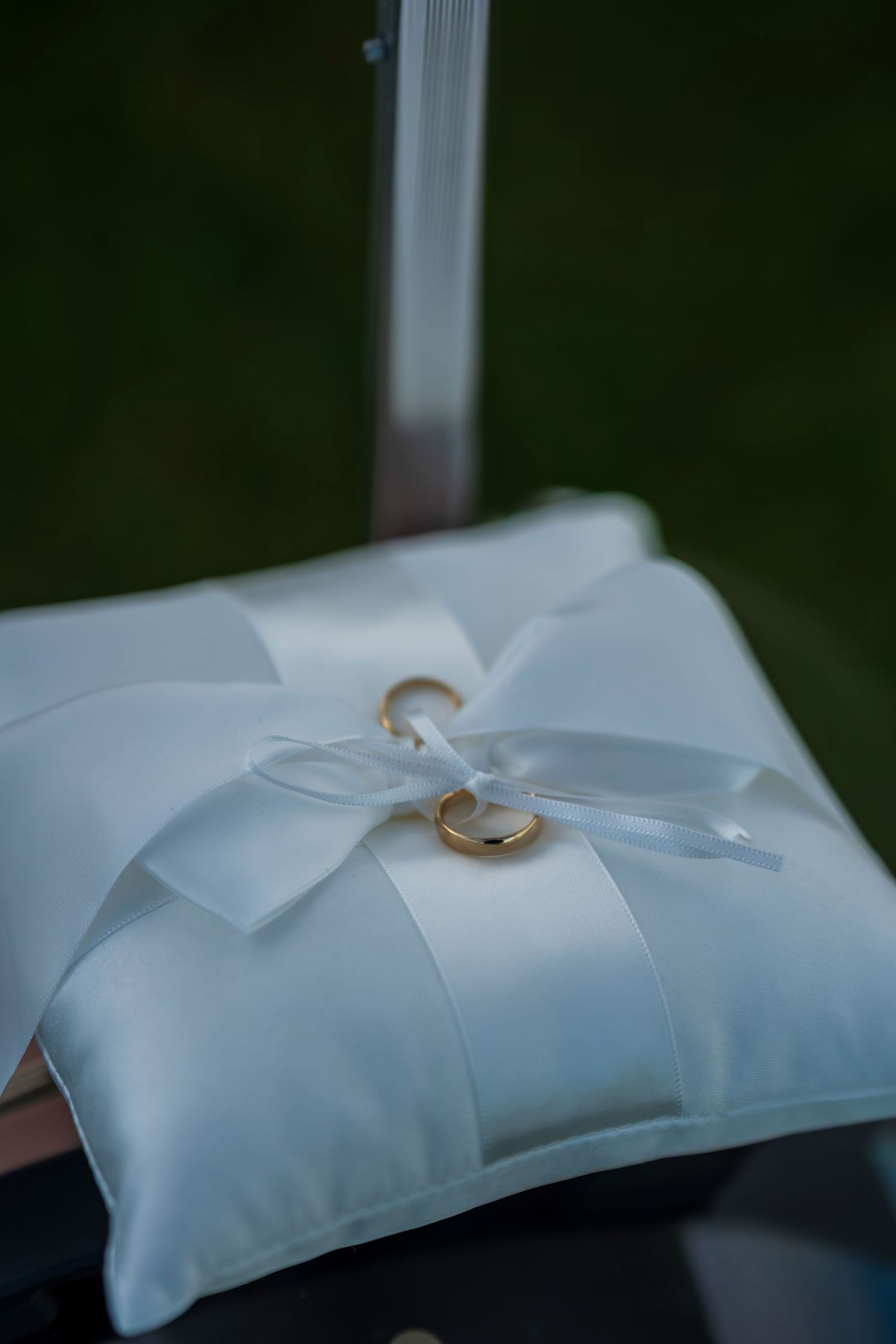 White satin ring bearer pillow with ribbon bow and wedding bands for ceremony.