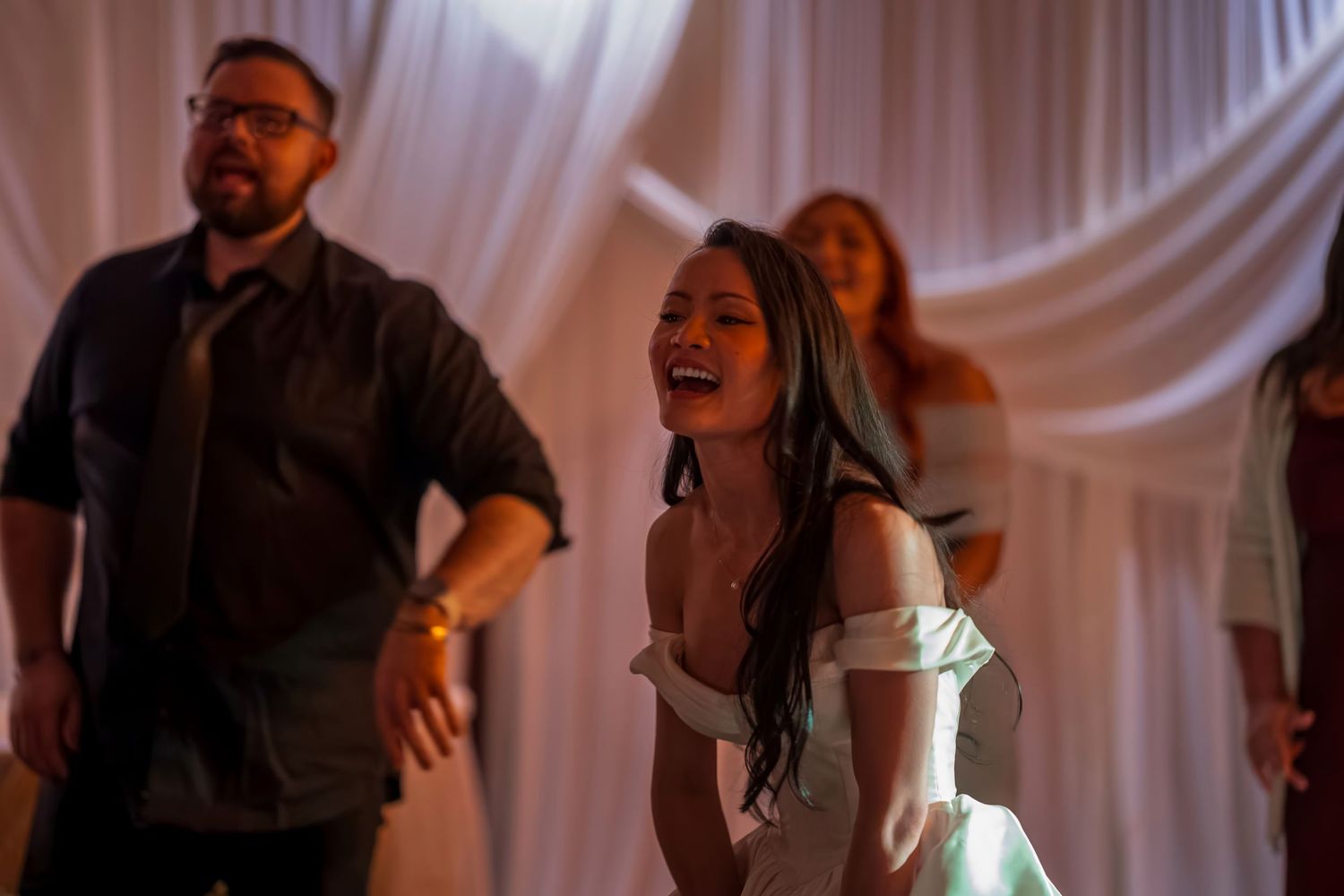 Wedding reception dance floor filled with celebrating guests in dim lighting.