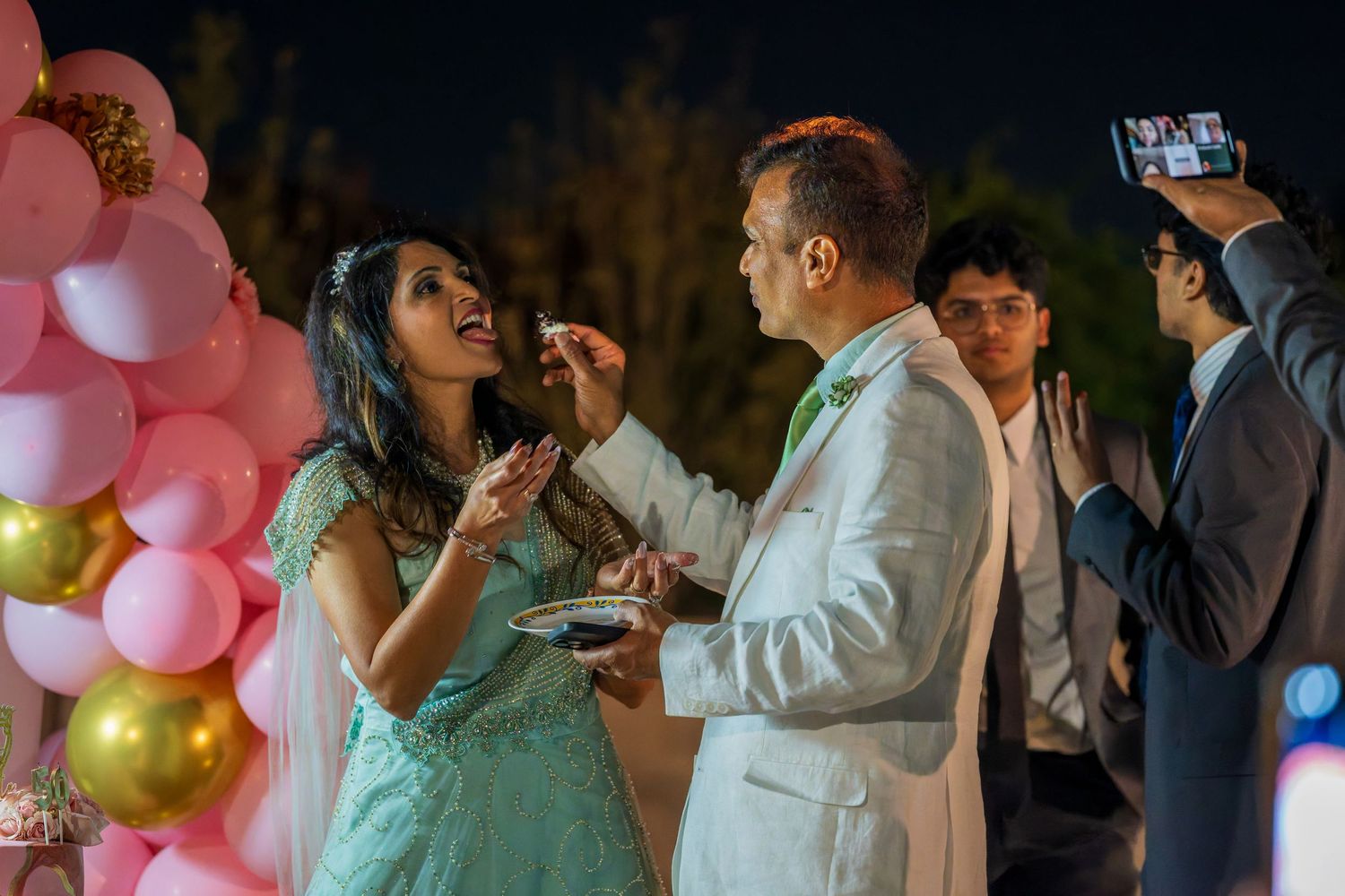 Couple sharing dessert near pink and gold balloon decorations at evening celebration.