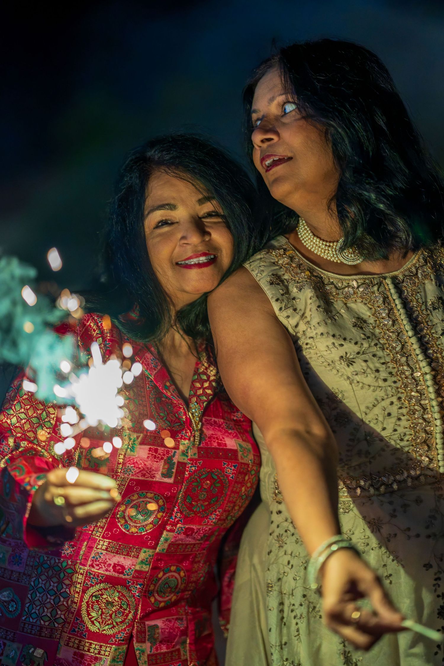 People in traditional Indian outfits hold sparklers during evening celebration.