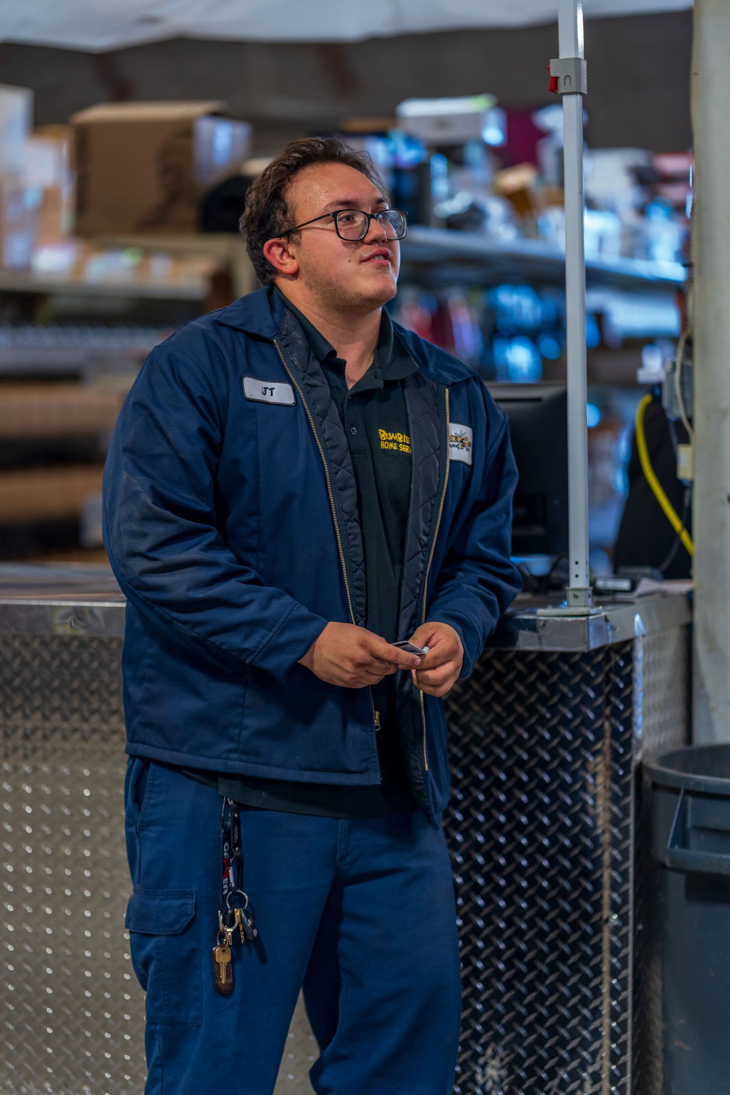 Employee in navy work uniform standing by equipment in warehouse setting.