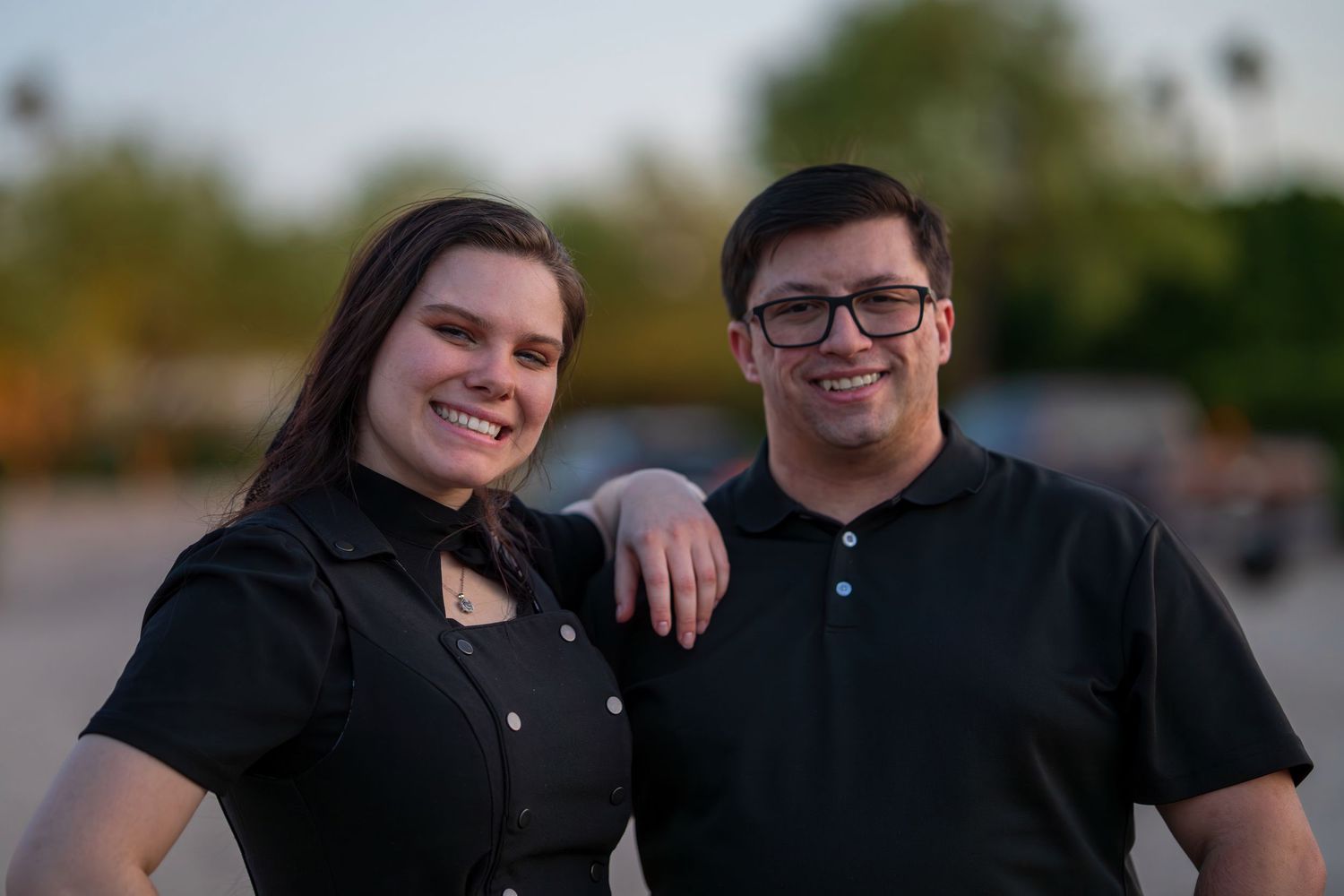 J and J in matching black outfits posing outdoors at sunset.