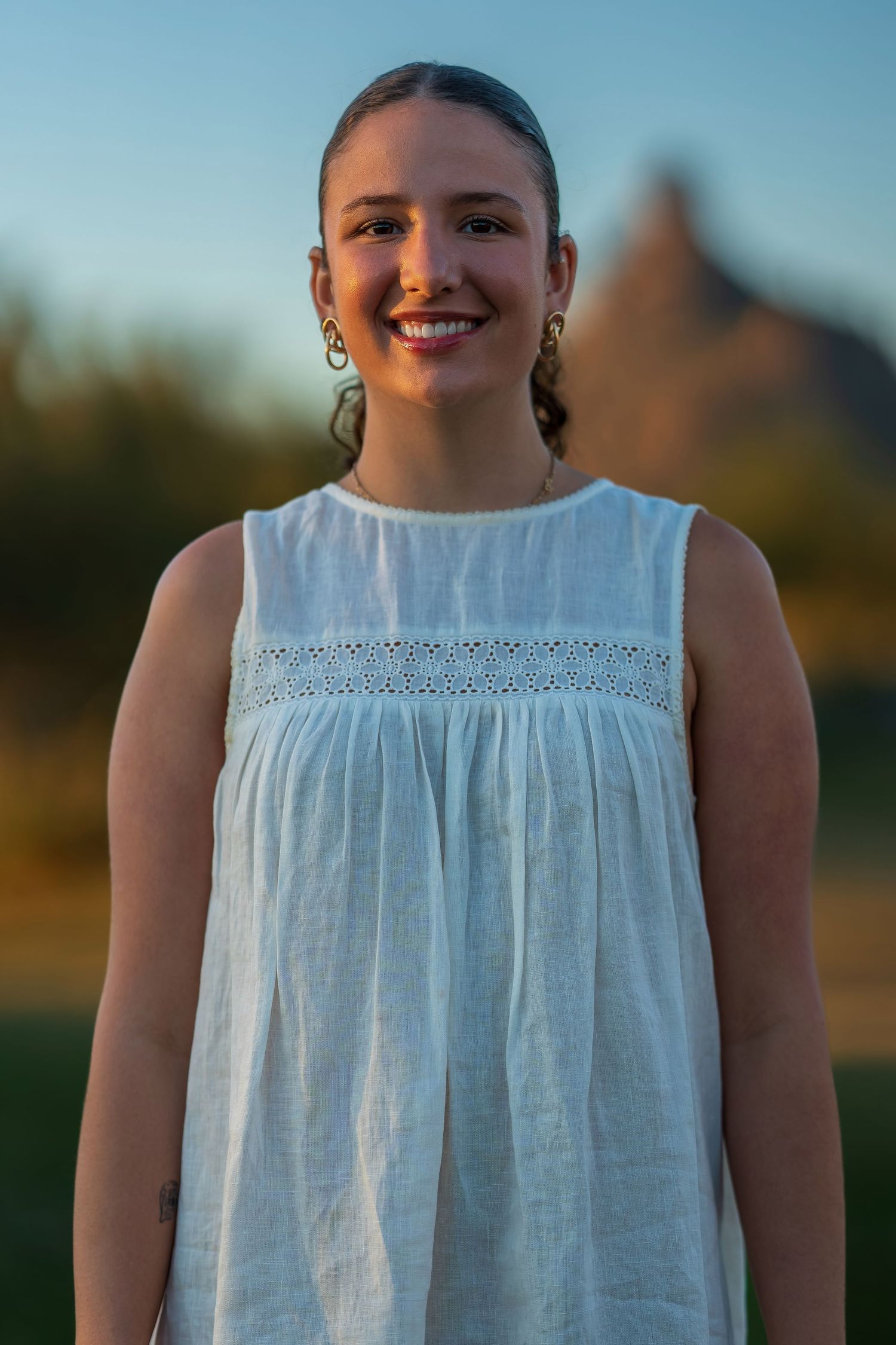 Portrait of person wearing white sleeveless dress with lace detail outdoors.