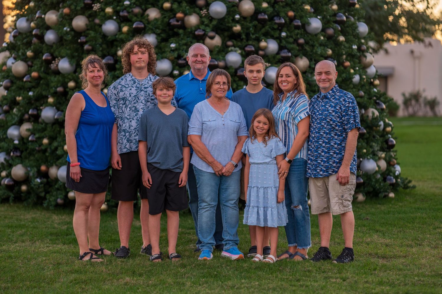 Group portrait with festive Christmas tree backdrop on grass lawn.