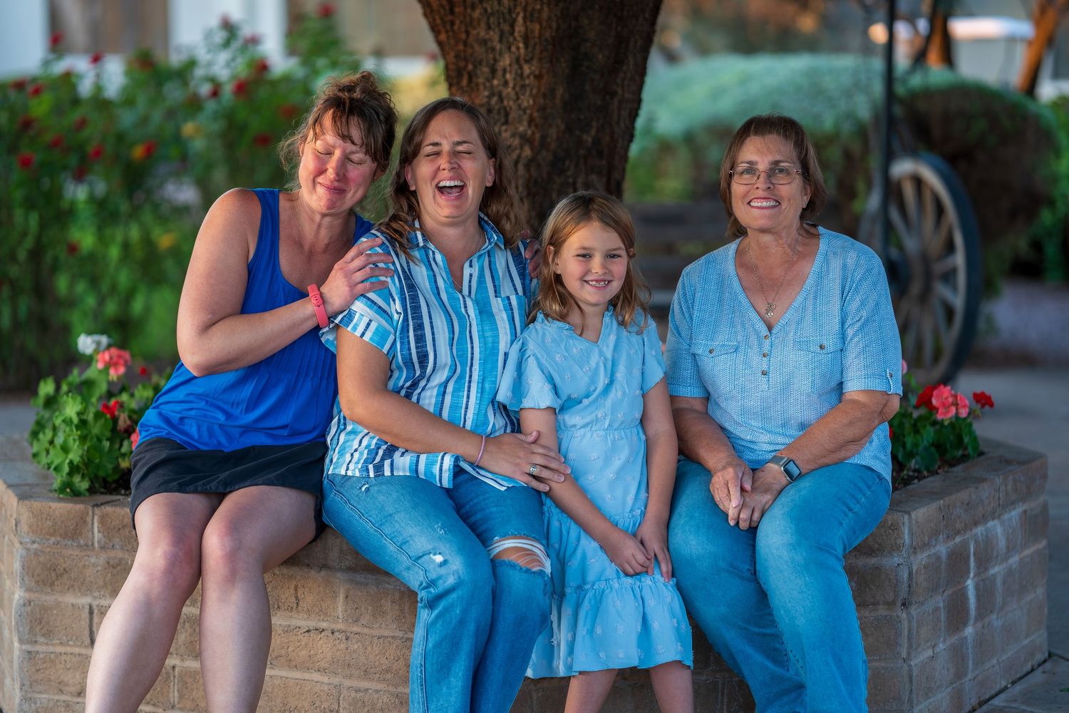 Family members sit together on brick steps under a large tree during sunset.