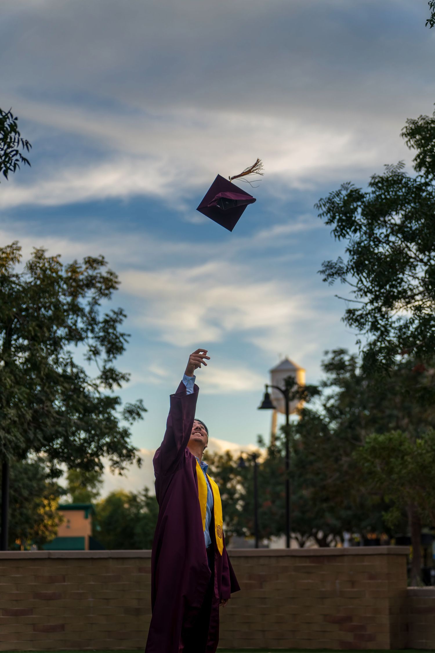 Graduate tosses cap in celebration against cloudy evening sky.