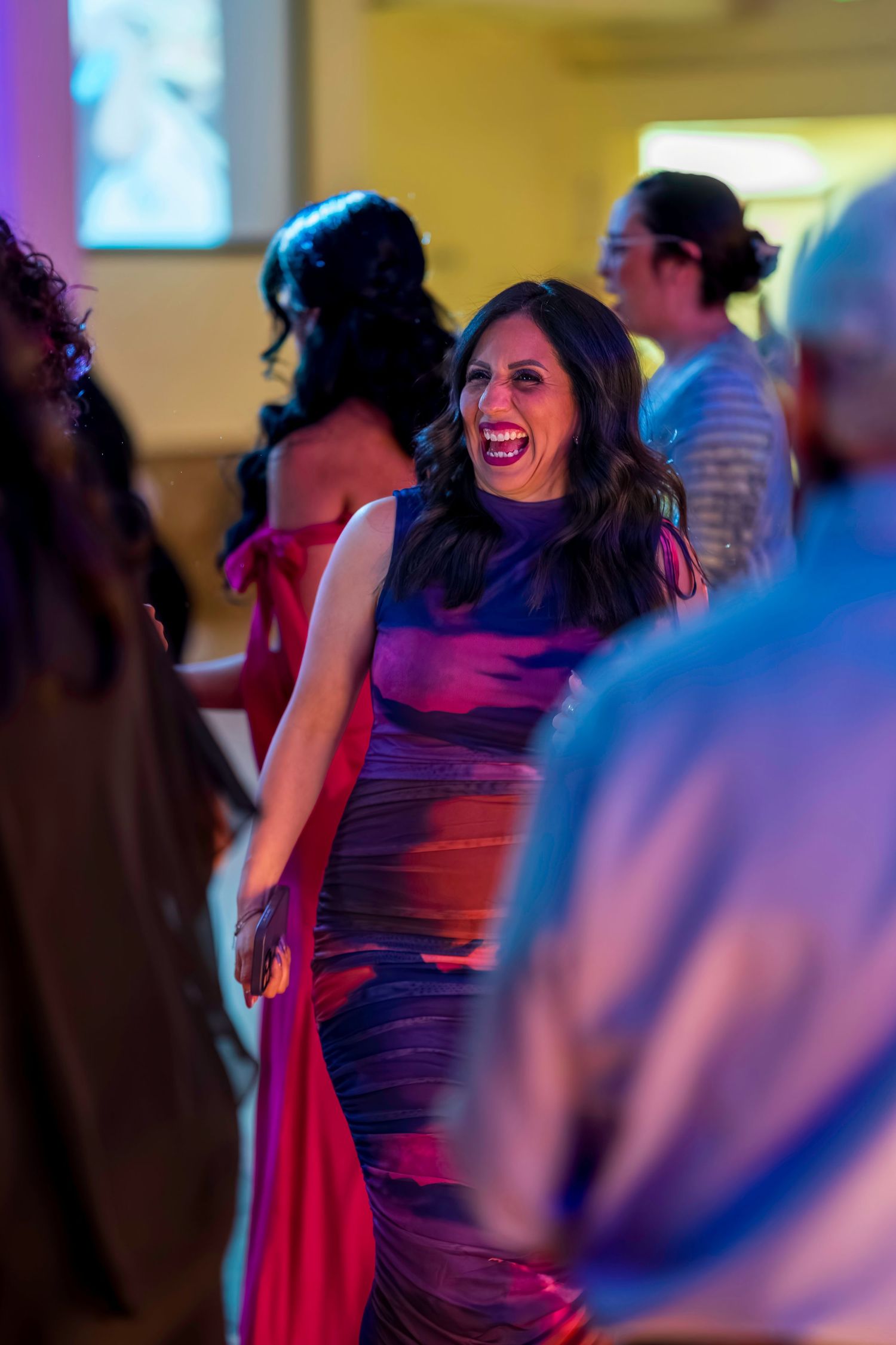 Woman in colorful gown laughing joyfully on a dance floor at an elegant evening event.