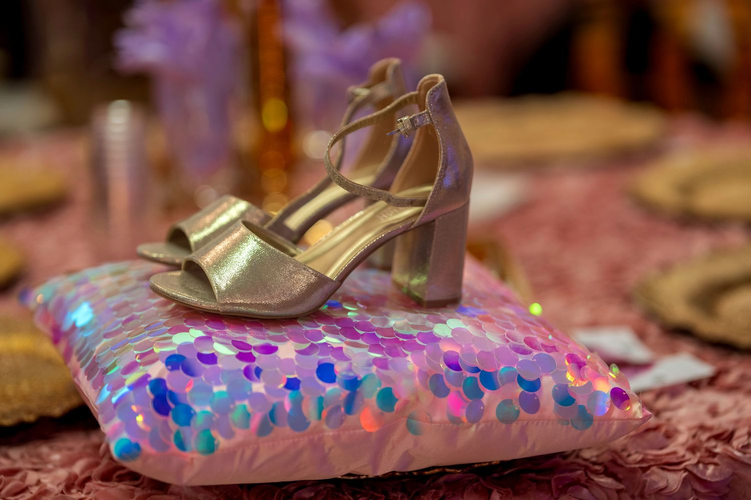 Gold strappy block heel sandals displayed on iridescent sequin pillow at a glamorous party.