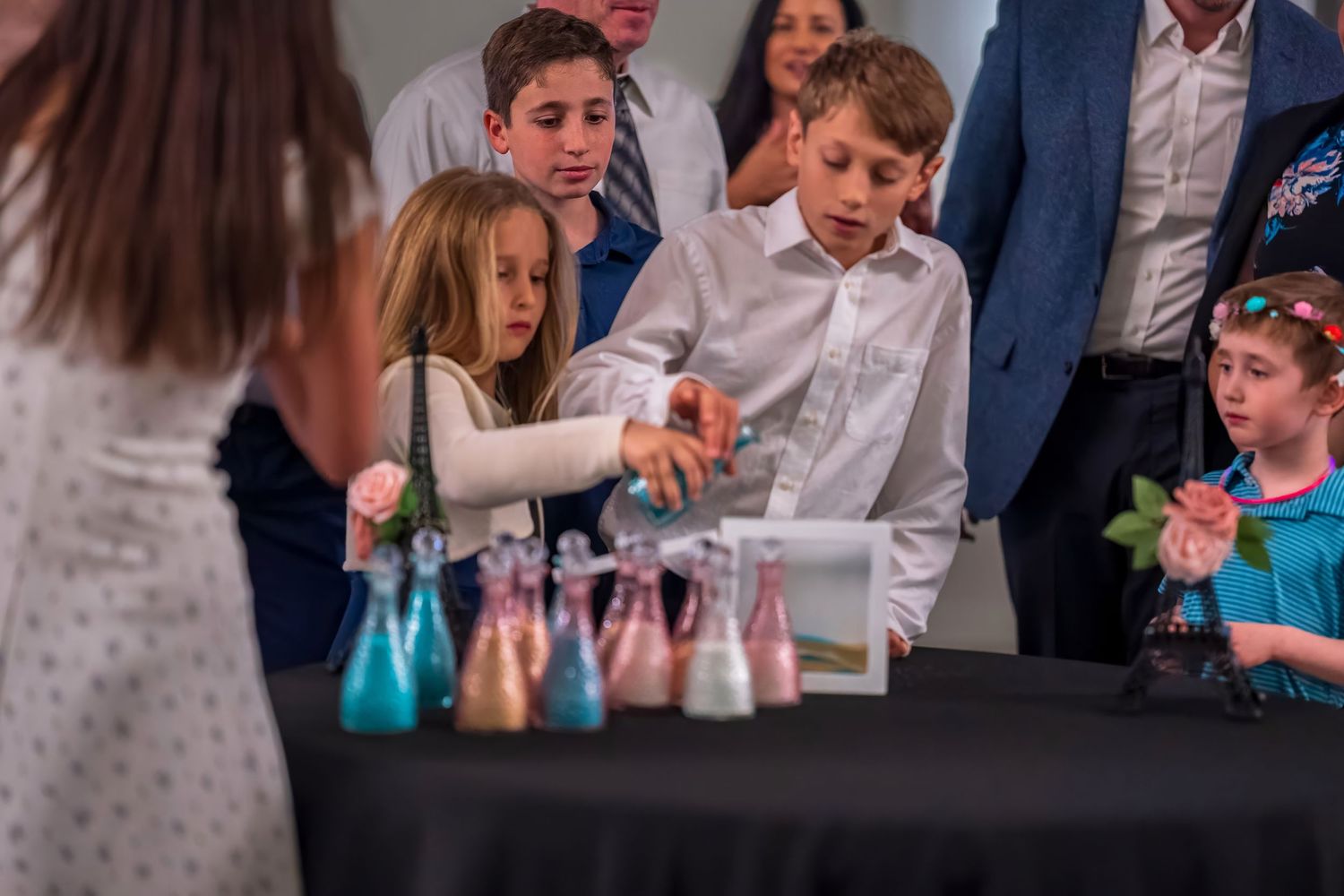 Children participate in a colorful sand art activity at a formal celebration event.