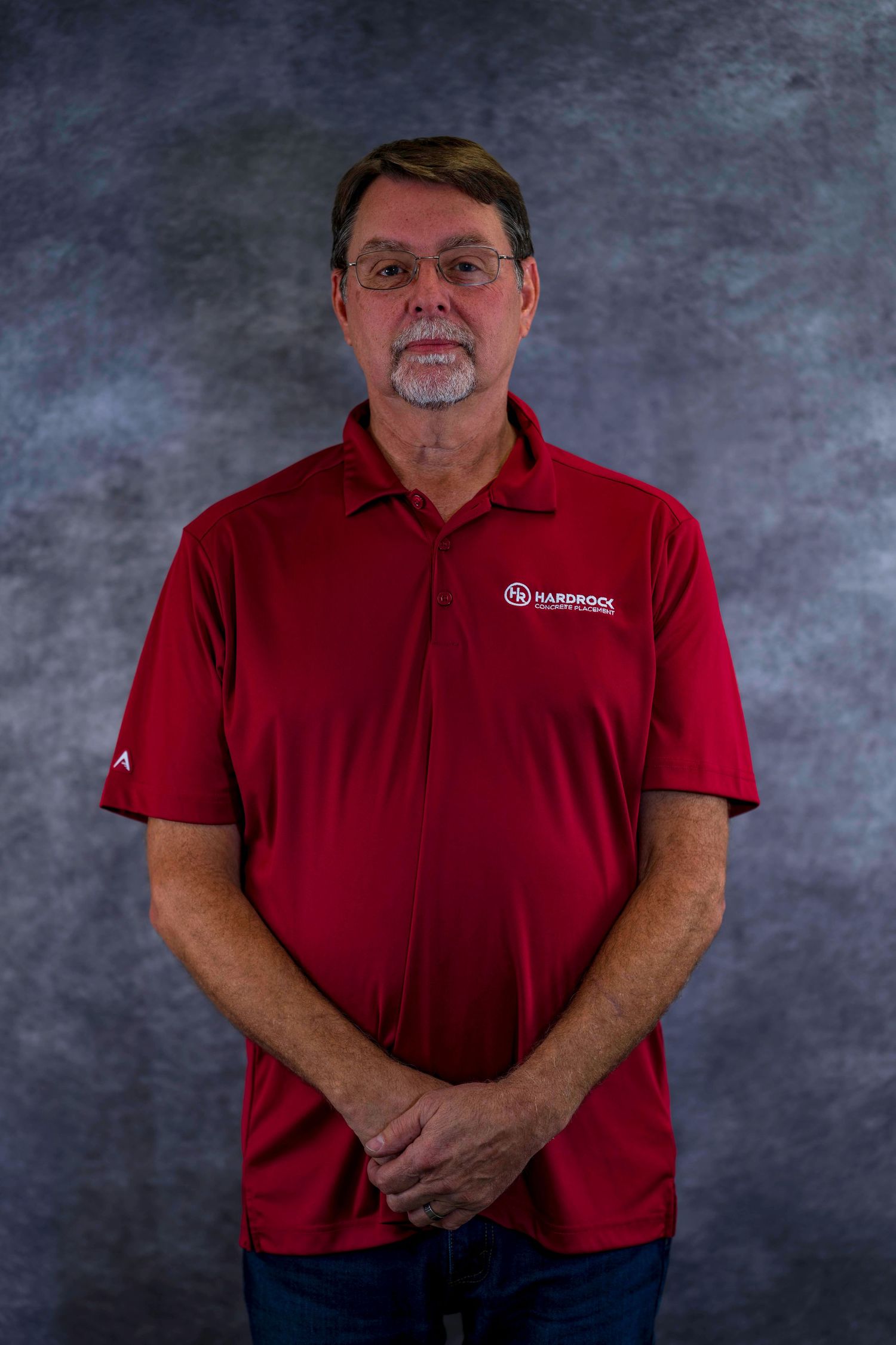 Professional portrait of person wearing red company polo shirt against textured backdrop.