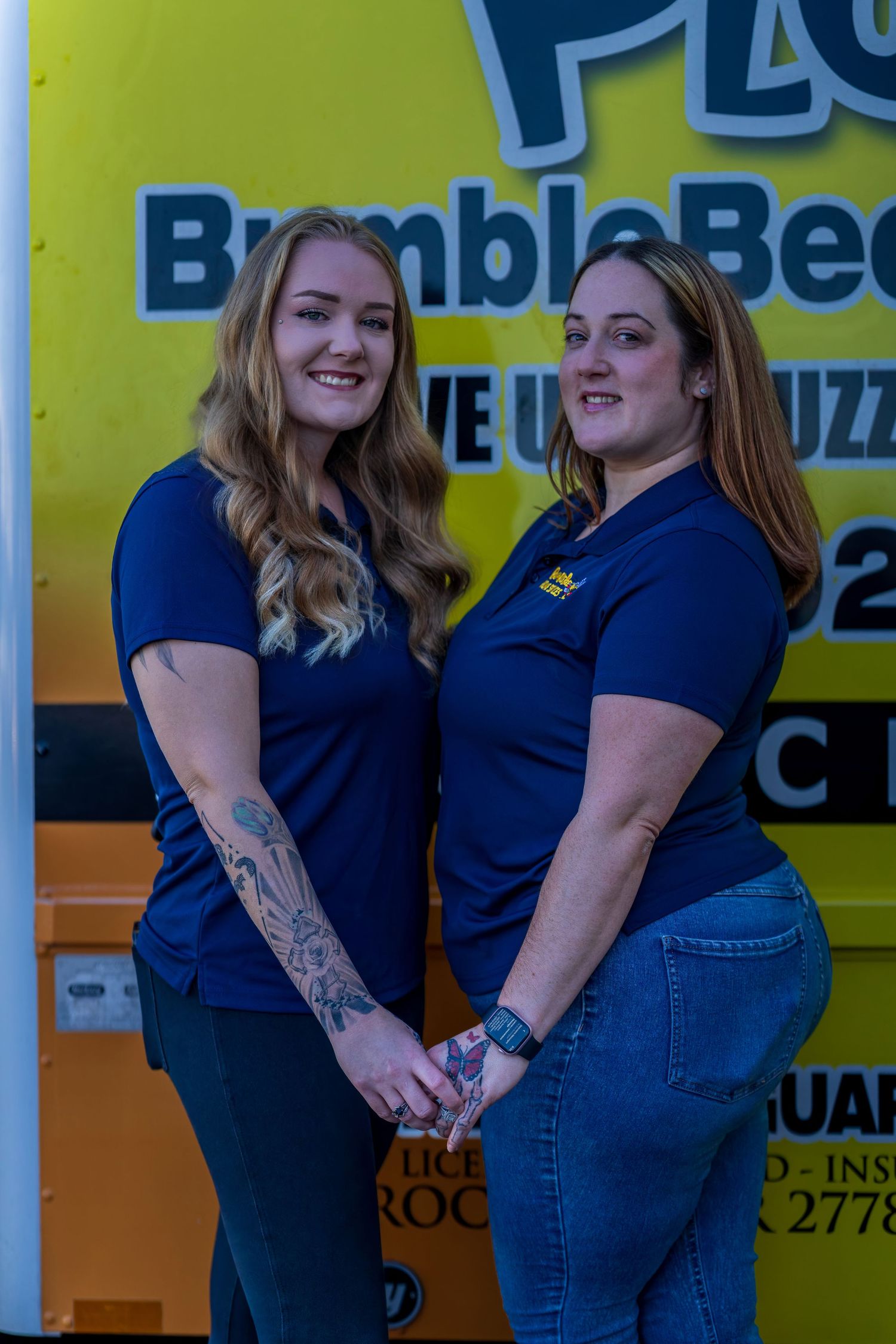 Two employees in navy uniforms pose in front of Bumble Bee company vehicle.