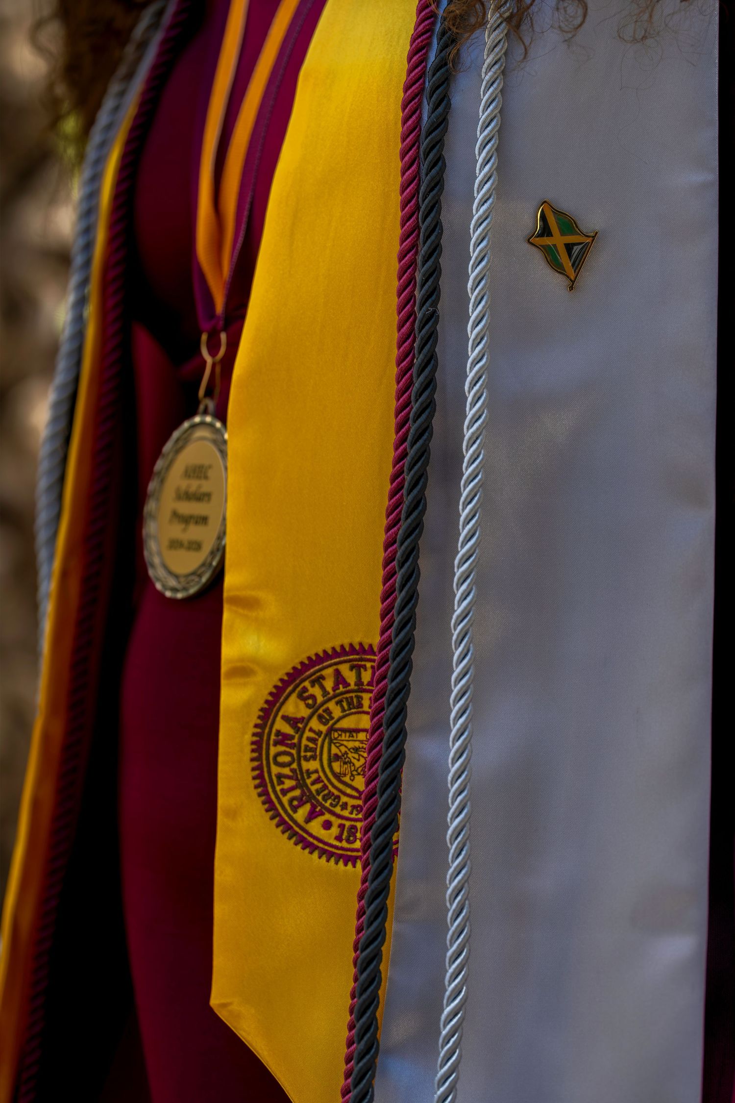 Arizona State University graduation regalia with gold stole, honor cord, medallion, and Jamaica pin on white gown.