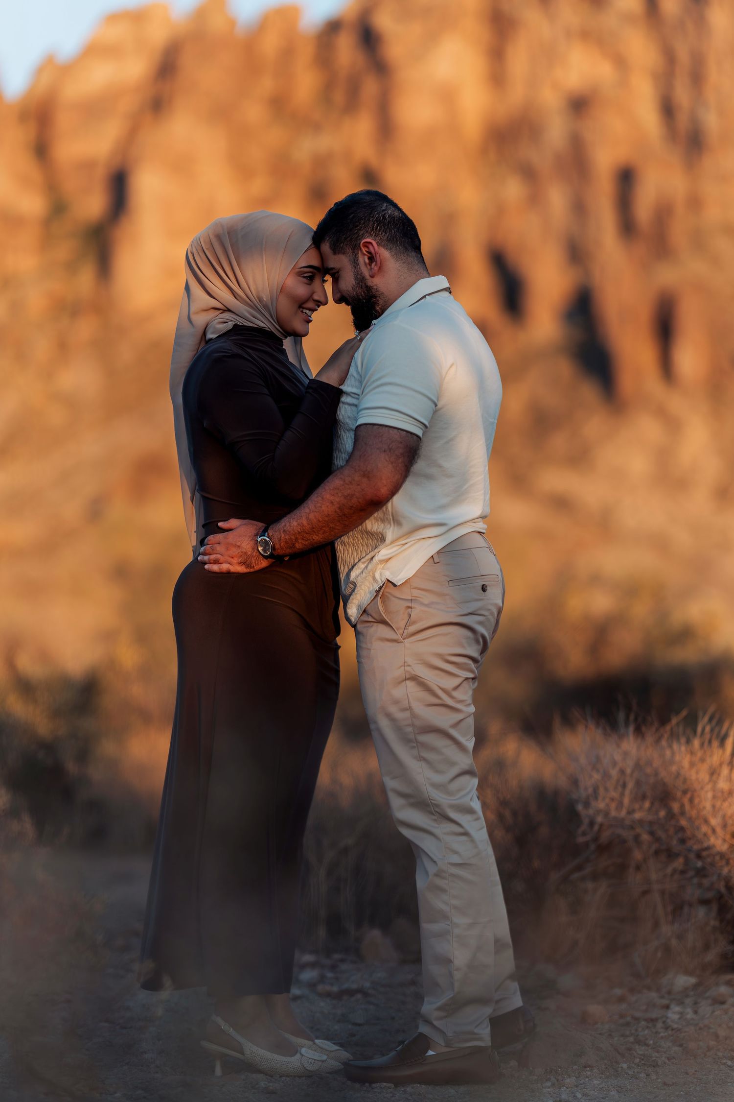 Romantic couple embracing at sunset with red rock canyon formations in the background, woman wearing hijab.