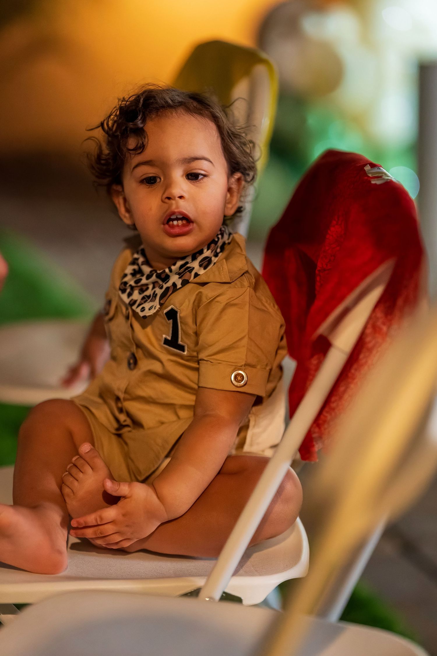 Young child in tan outfit with leopard print collar sits in chair at event.