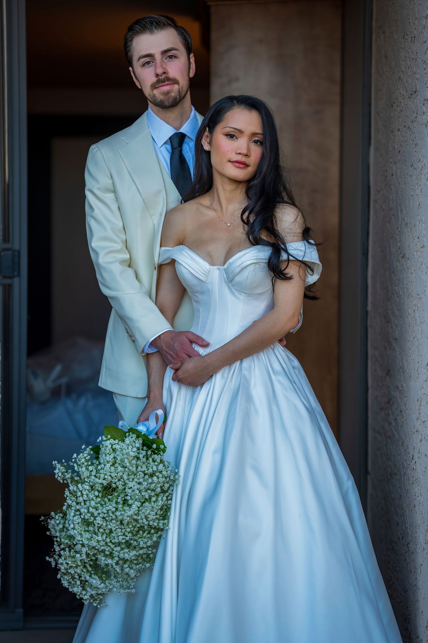 A wedding couple poses with baby's breath bouquet in classic cream and white formal wear.