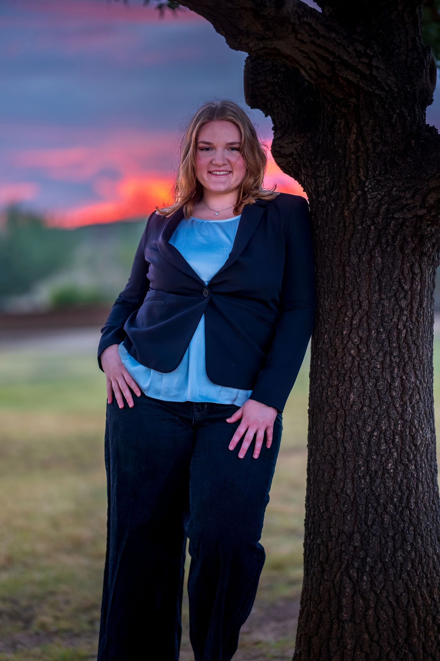 Professional photoshoot against vibrant sunset sky and tree silhouette.