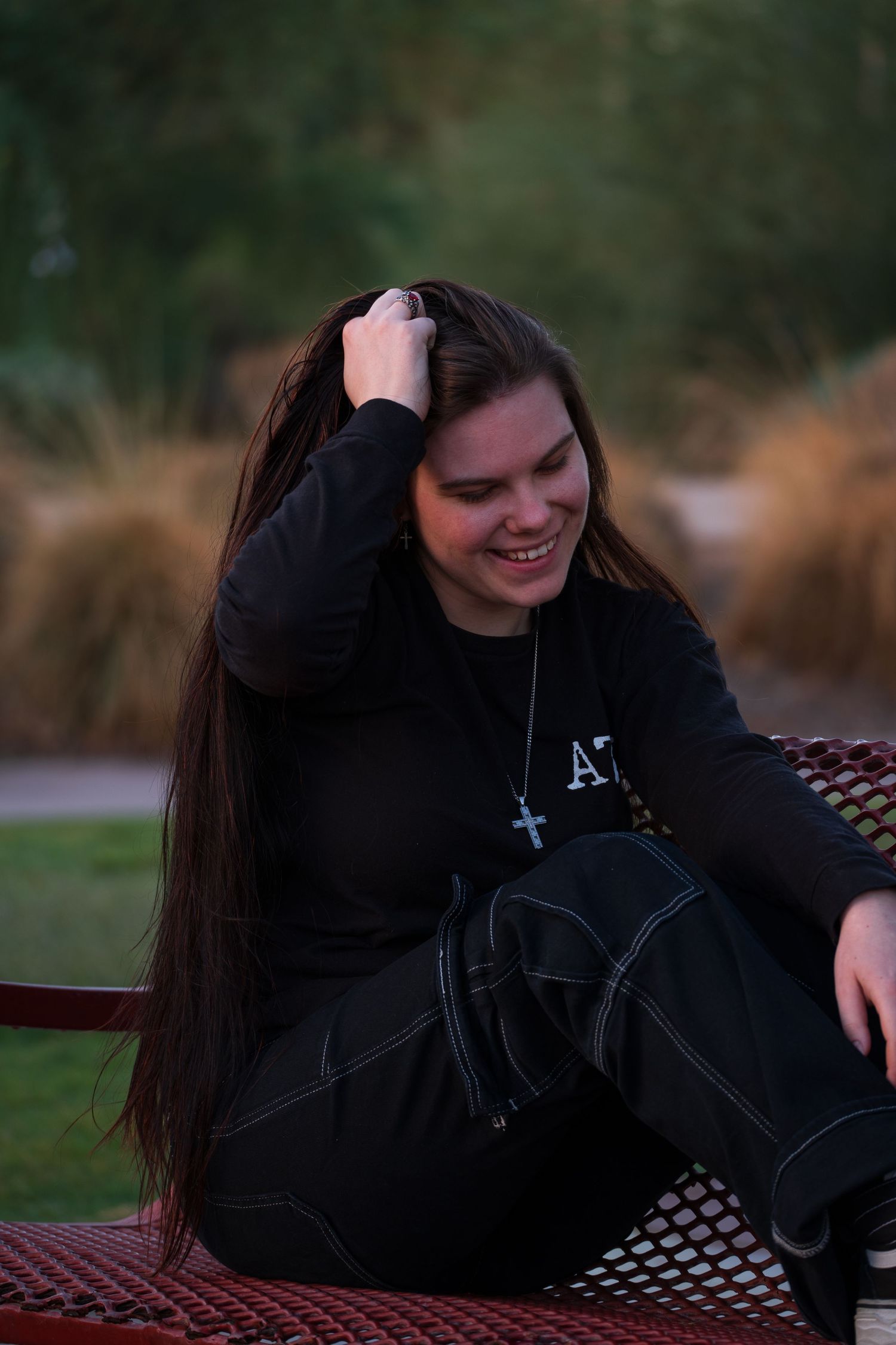 Natural outdoor portrait showing relaxed pose on metal bench with dark attire.