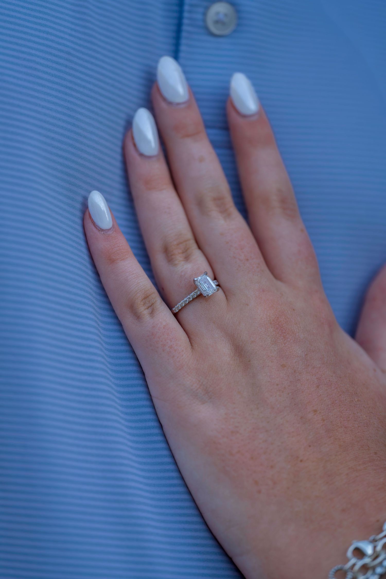 Close-up of an engagement ring with emerald-cut diamond on a hand with white manicured nails.