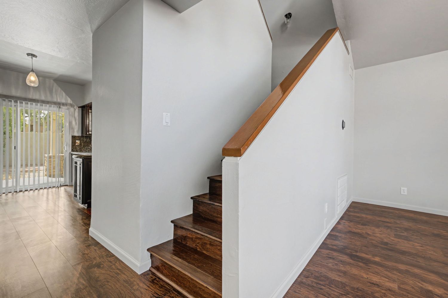 Bright home interior featuring hardwood floors, white walls, and a wooden staircase leading to the upper level.