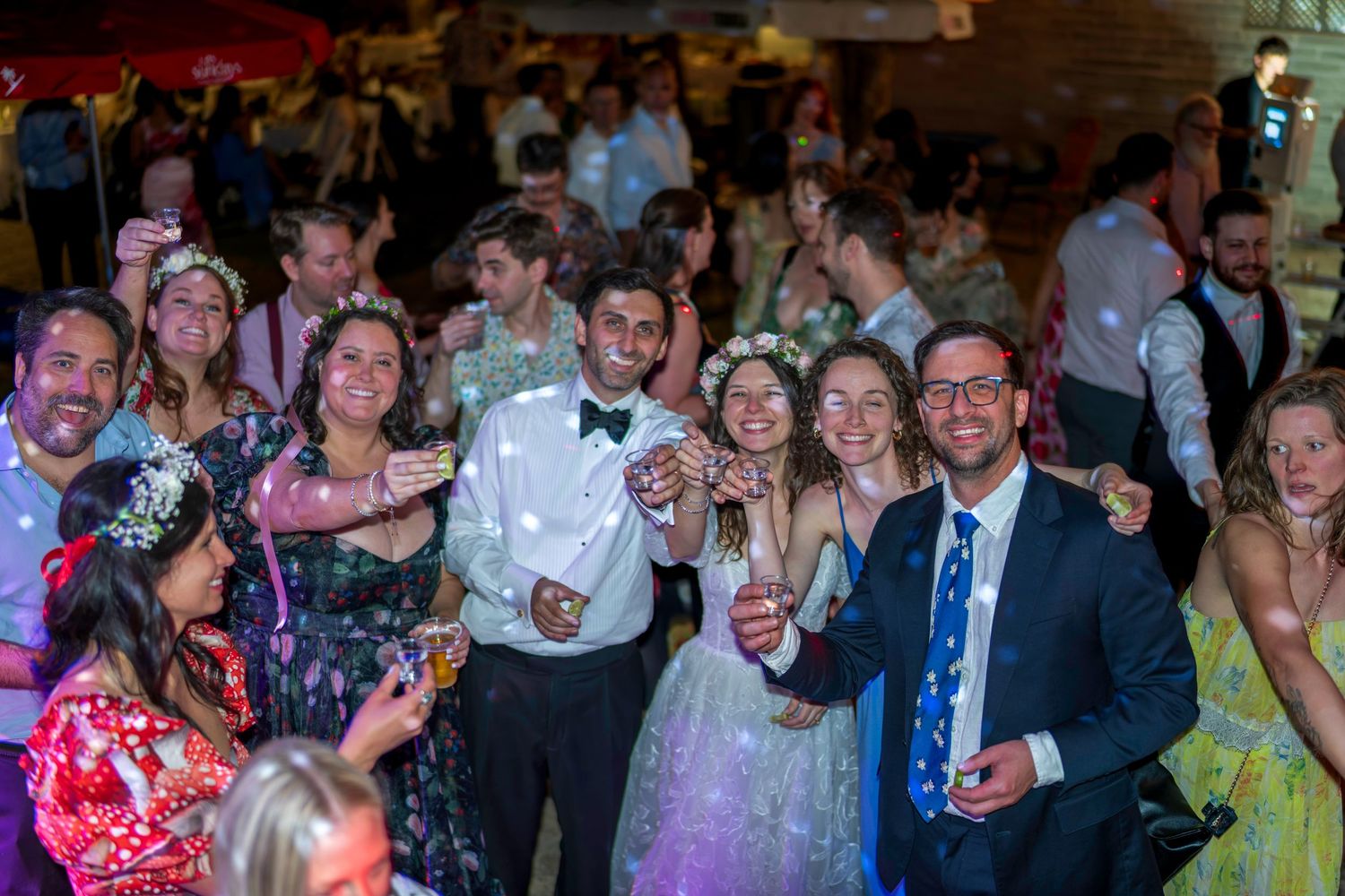 Joyful wedding reception guests celebrating on the dance floor, with bride in white gown and groom in bow tie.