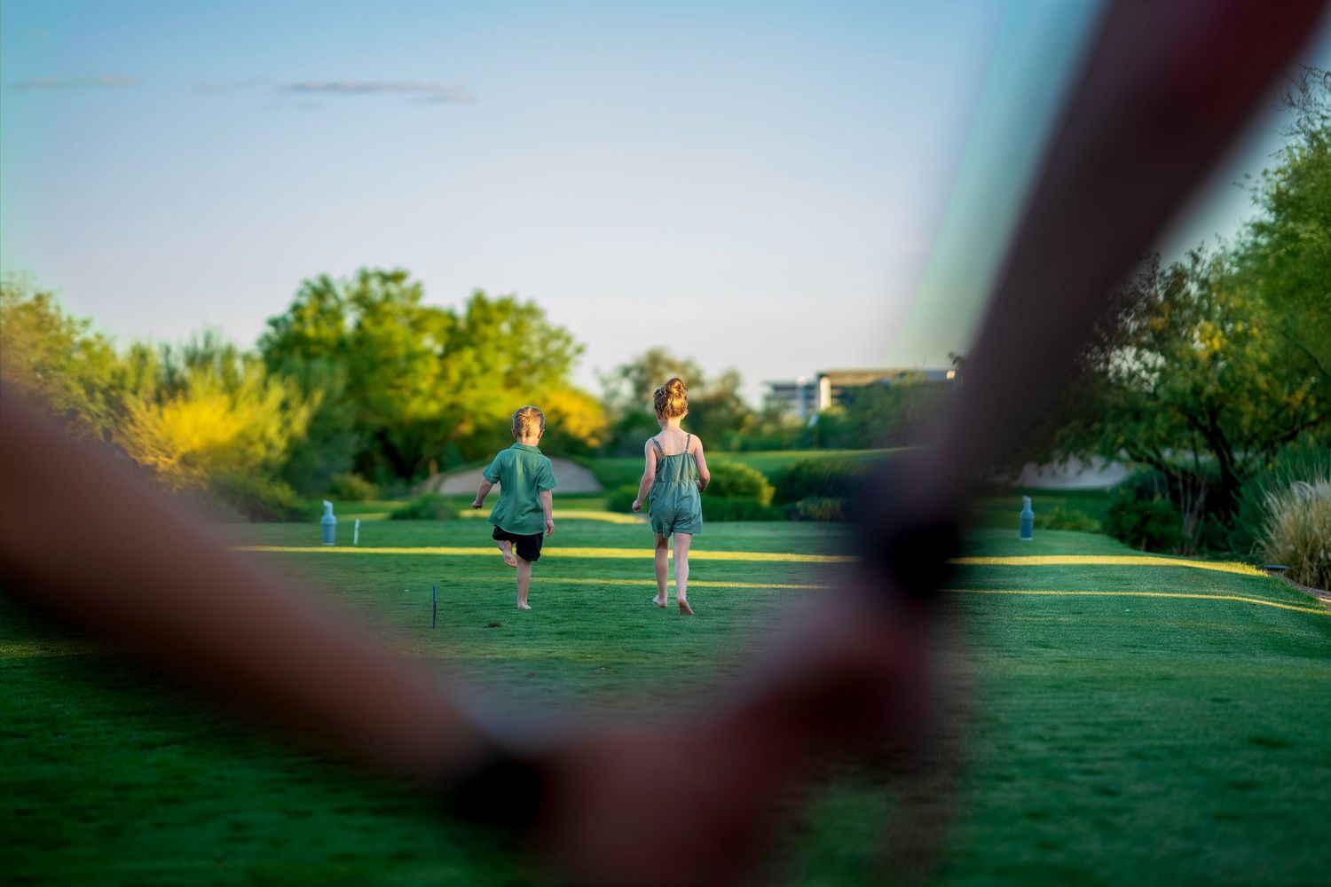 Two children running across green grass field at sunset in a scenic outdoor park setting.