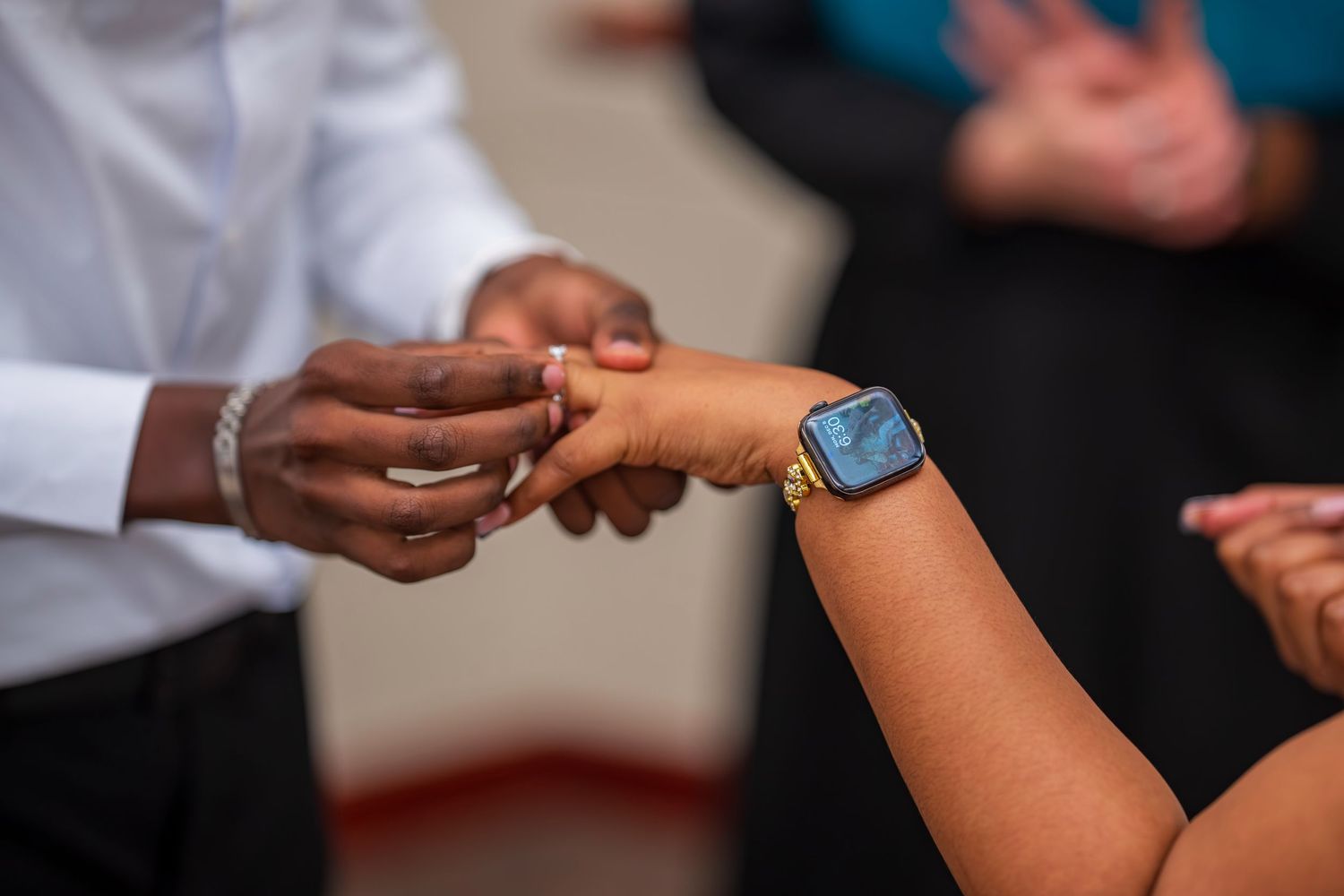 Close-up of a man placing a ring on a woman's finger during a wedding ceremony, bride wearing a gold smartwatch.