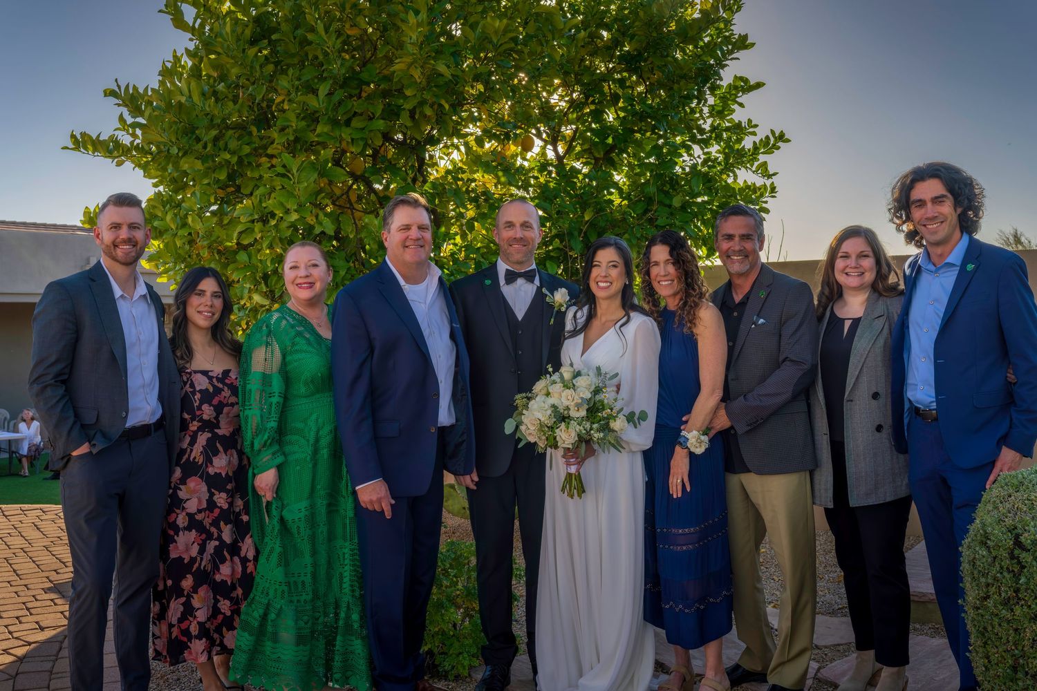 Wedding party group portrait of ten guests and newlyweds smiling outdoors at golden hour.