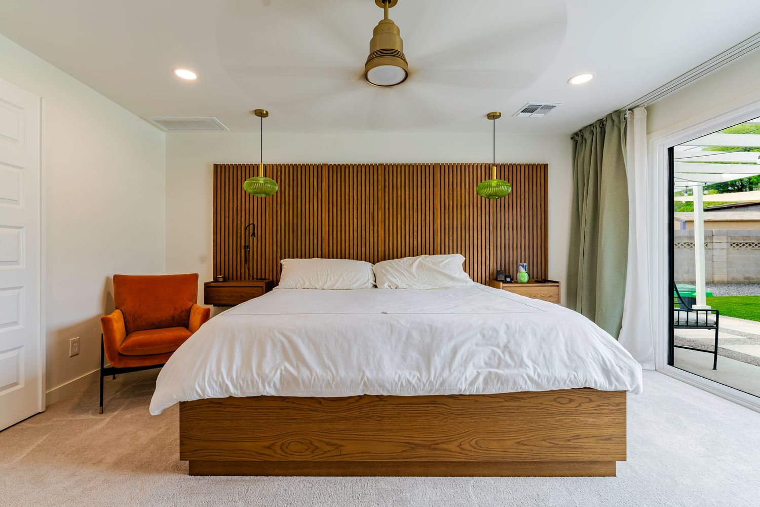 Mid-century modern bedroom with wood panel headboard, white bedding, green pendant lights, and sliding glass door.