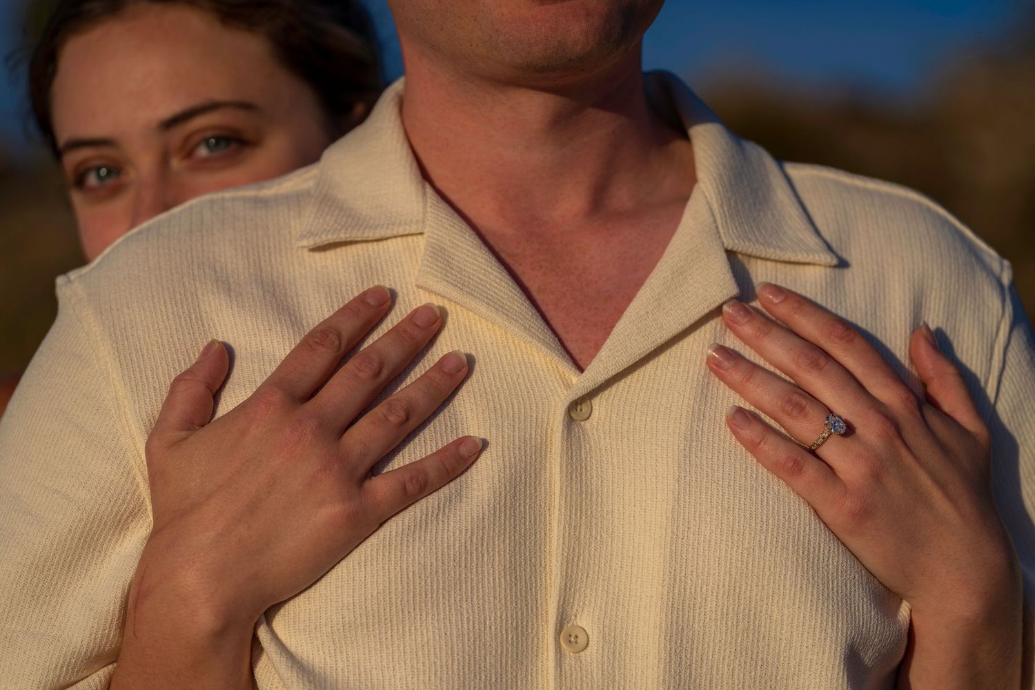 Close-up of a woman wrapping her arms around a man in a white shirt at golden hour.