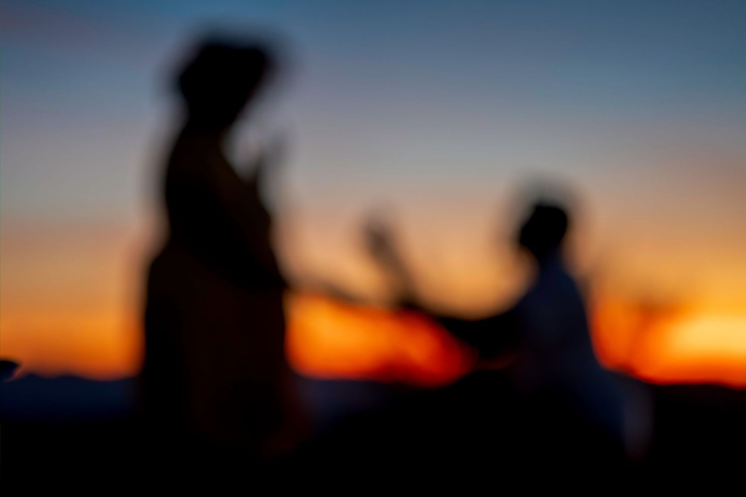 Silhouette of couple at vibrant orange and blue sunset, man kneeling in romantic proposal scene.