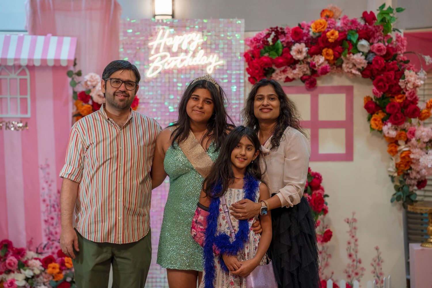 A family gathering in front of a pink floral wall with decorative elements at a celebration.