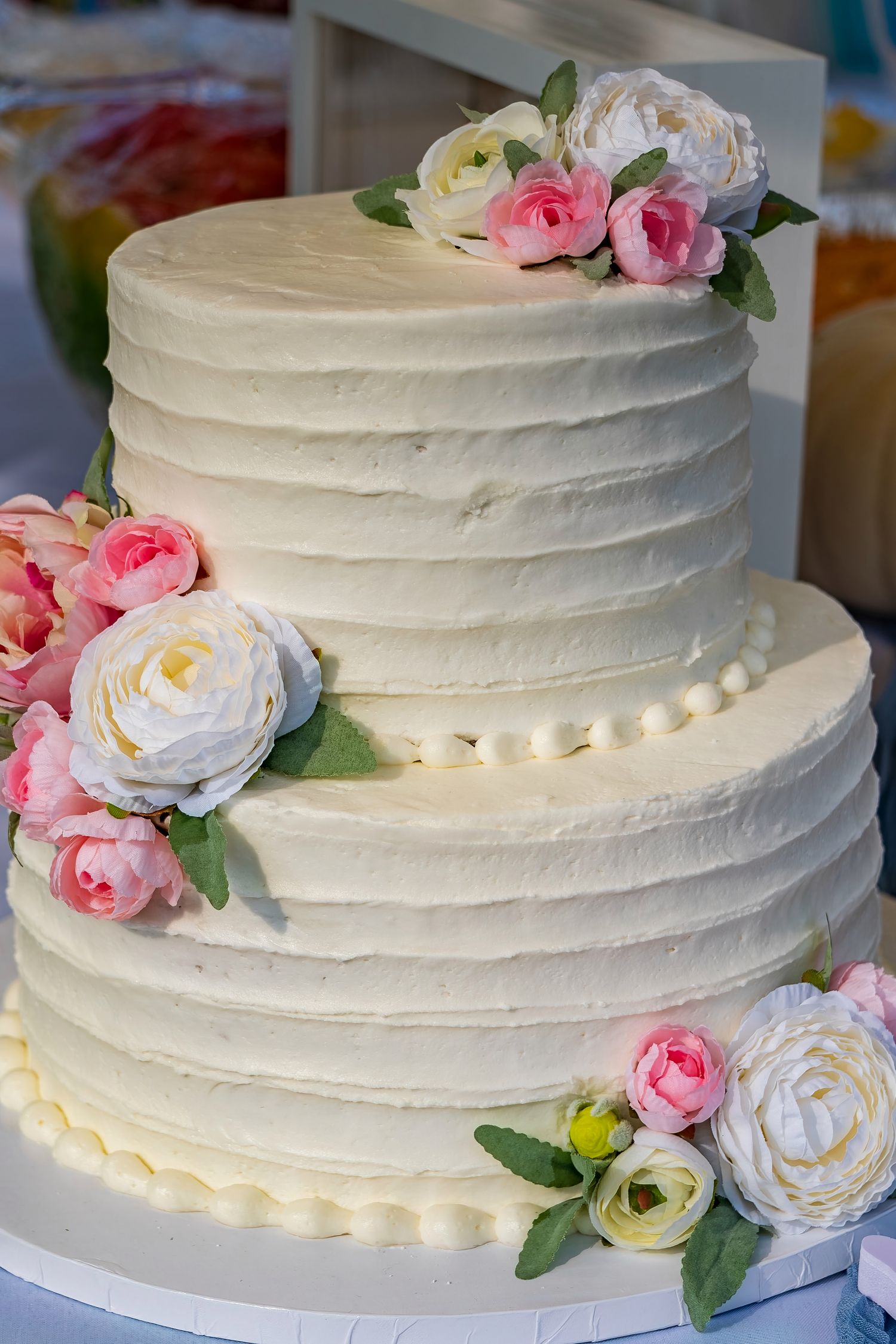 White wedding cake decorated with pink and white roses and delicate frosting details.