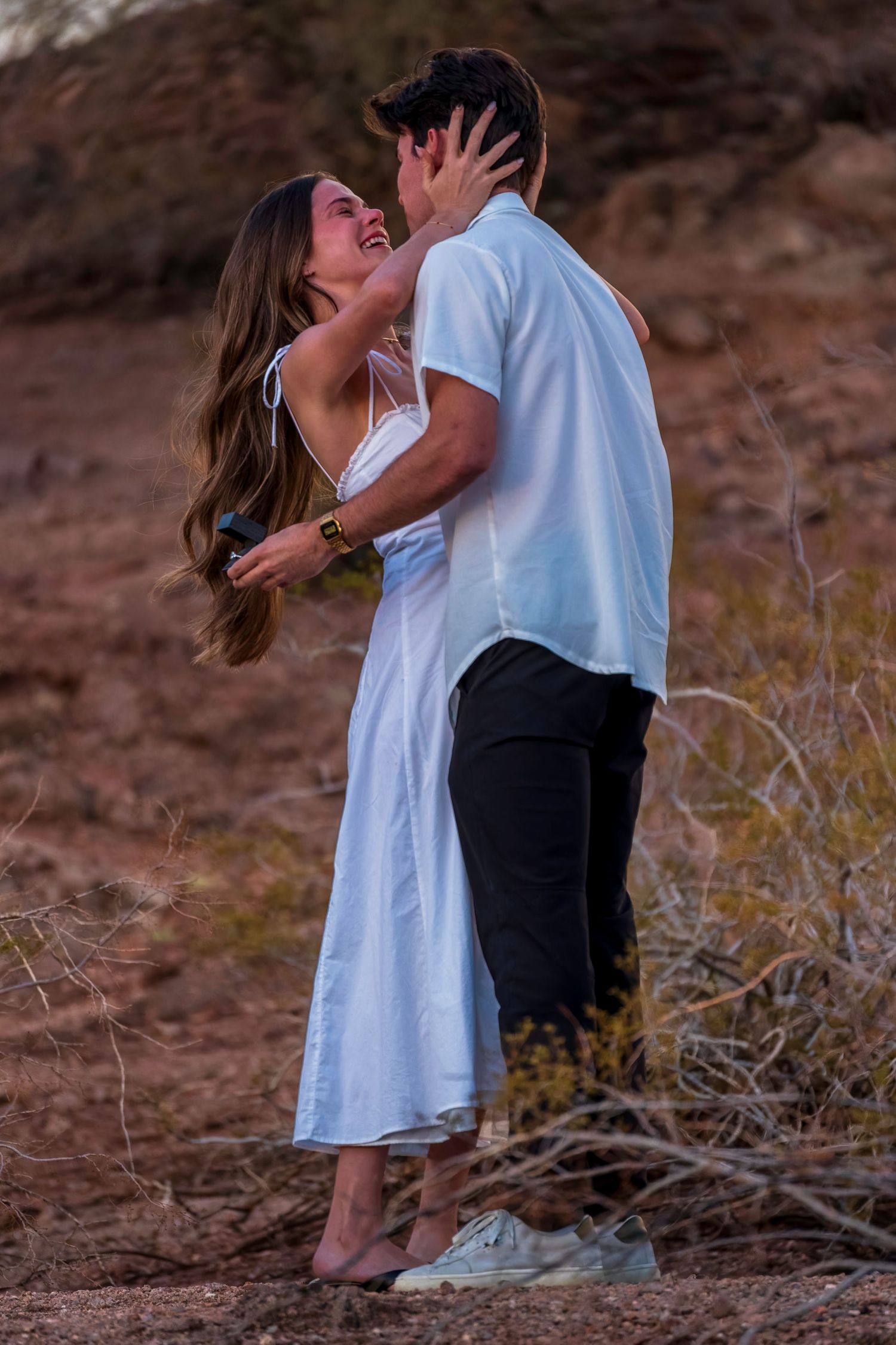 Couple in white and black attire sharing a romantic moment on rocky terrain.