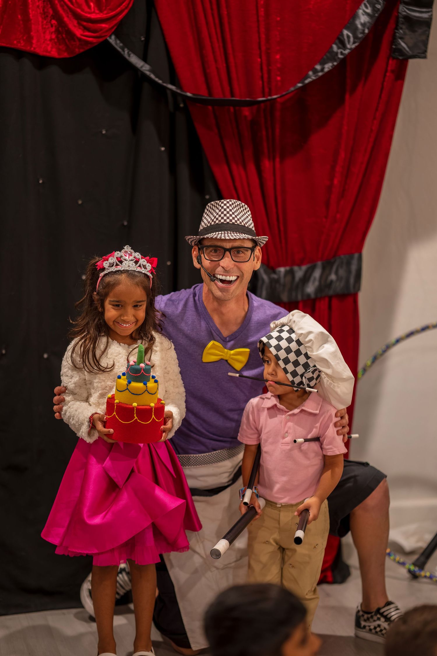 Magic show performance featuring performers in colorful costumes against a red curtain backdrop.