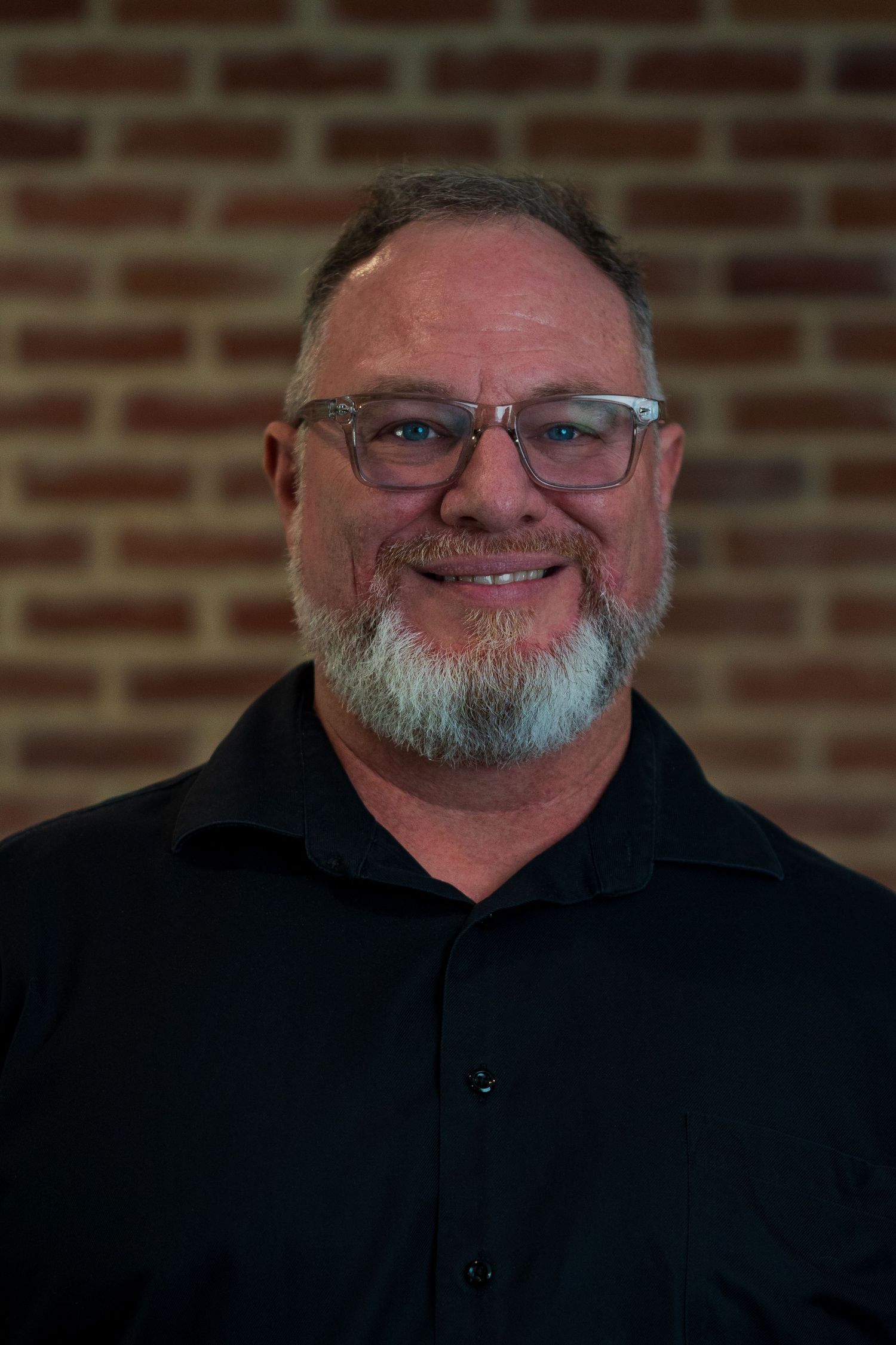 Portrait of a person in black attire against a brick wall background.